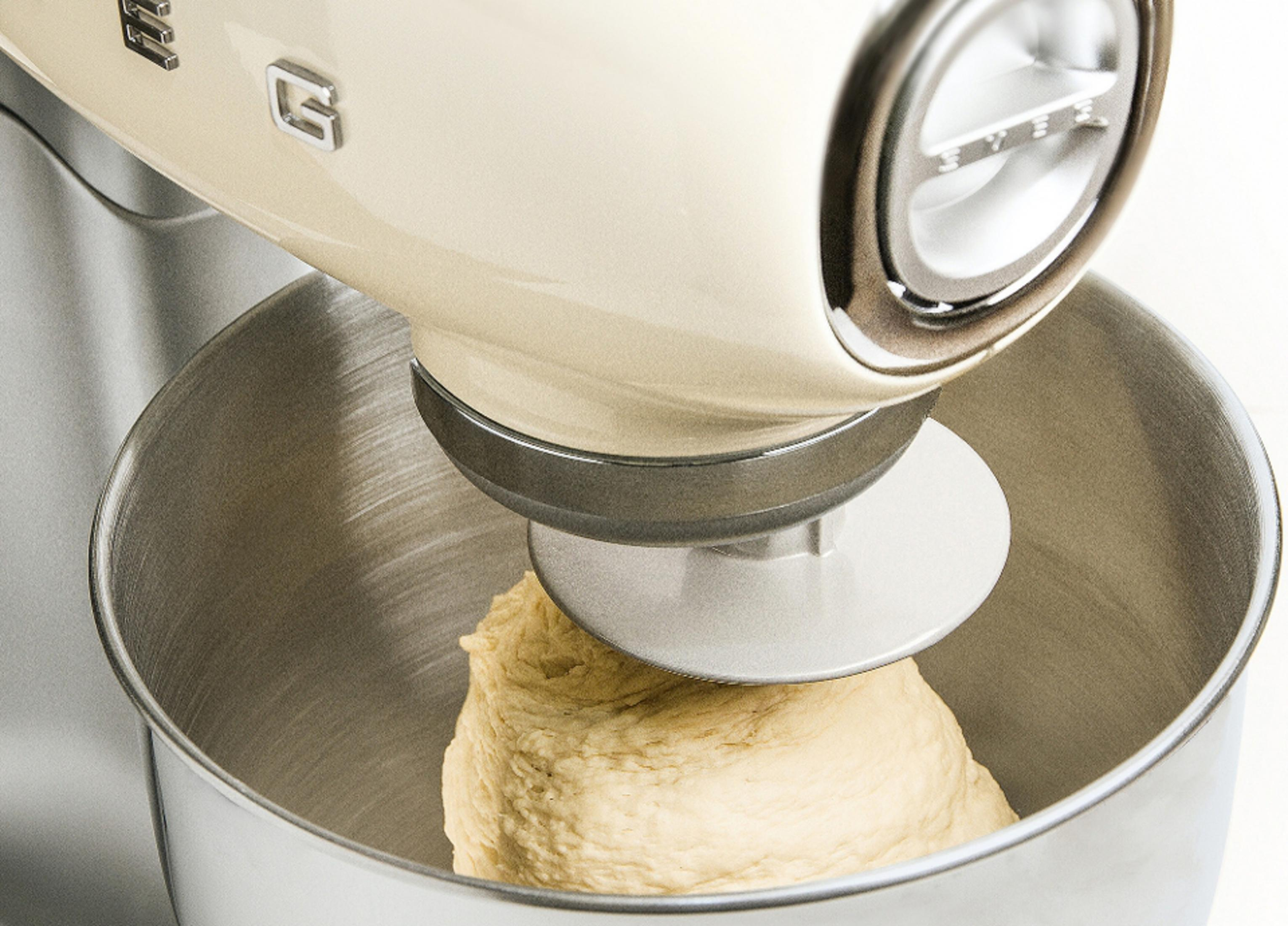 Un robot da cucina color crema con gancio impastatore che lavora l'impasto in una ciotola inox.