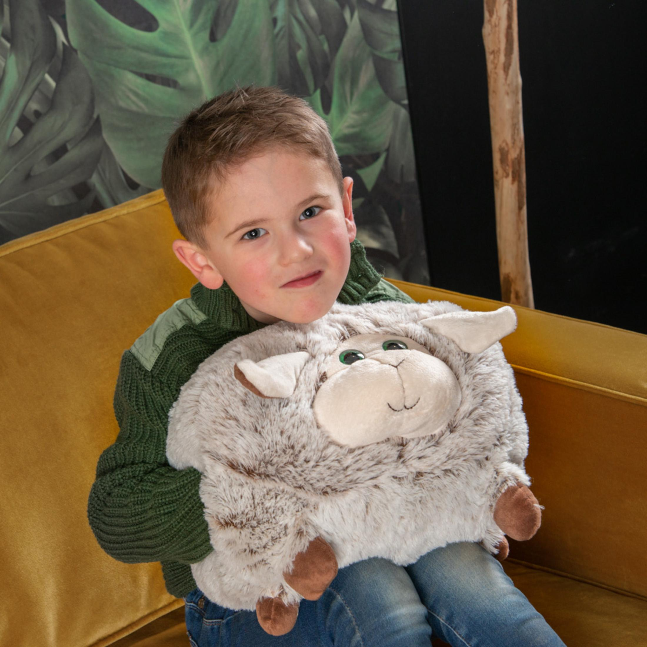 Ein Junge mit einem Schaf-Plüschtier sitzt auf einem gelben Sofa vor einer Blattwand.
