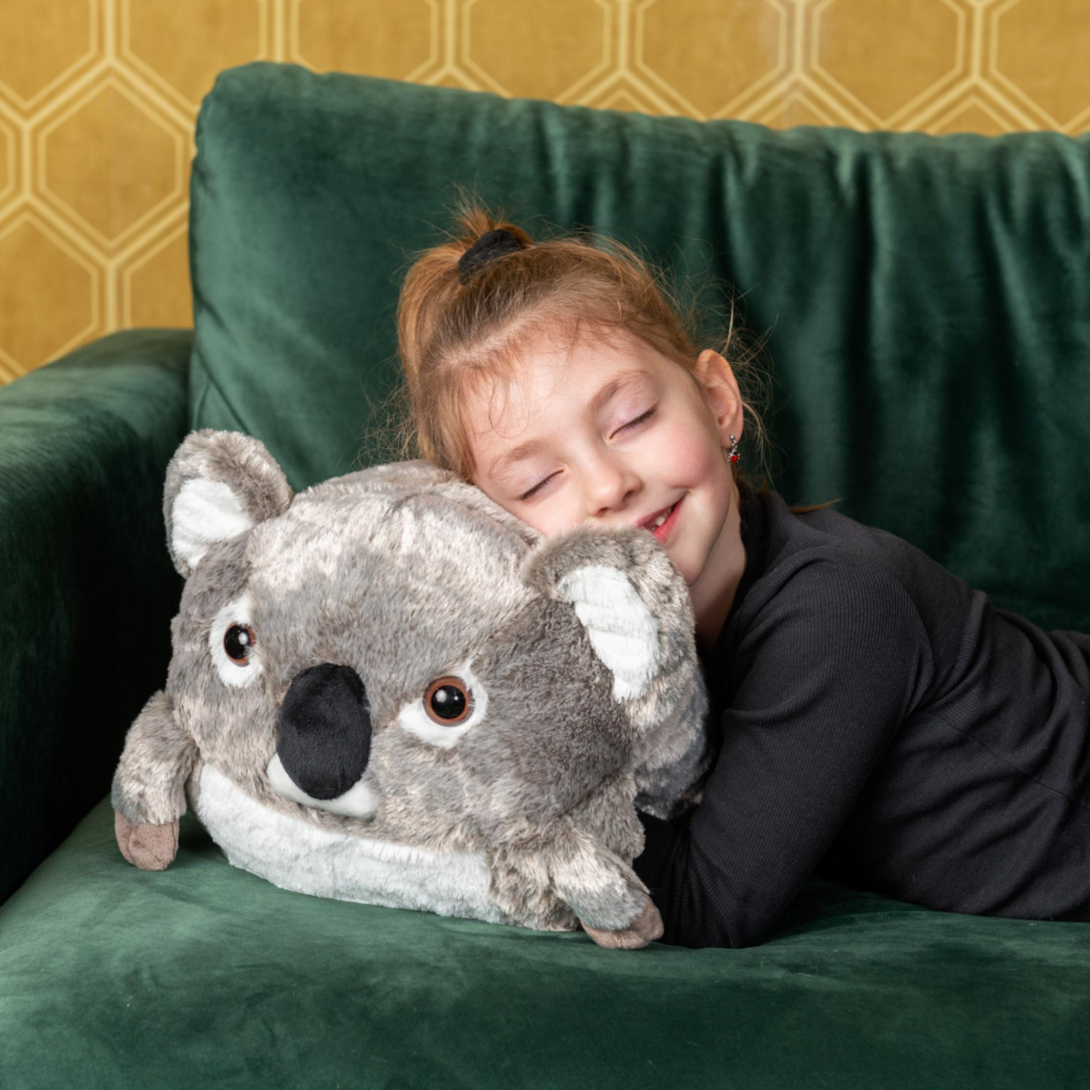 Ein Mädchen liegt auf einer grünen Couch und umarmt ein Koala-Kuscheltier.