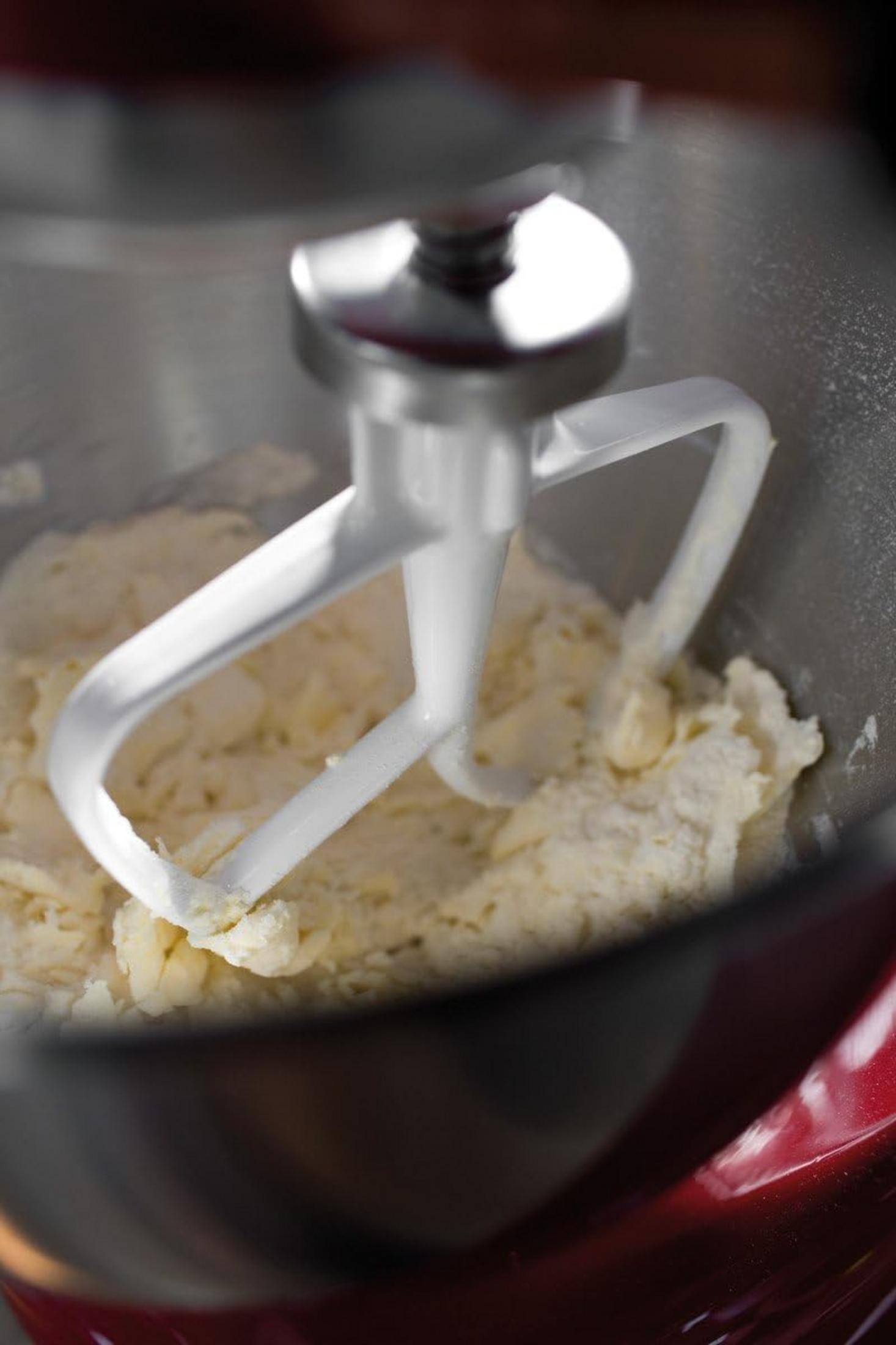 Ein weißer Flachrührer mischt cremigen Teig in einer roten Küchenmaschine.