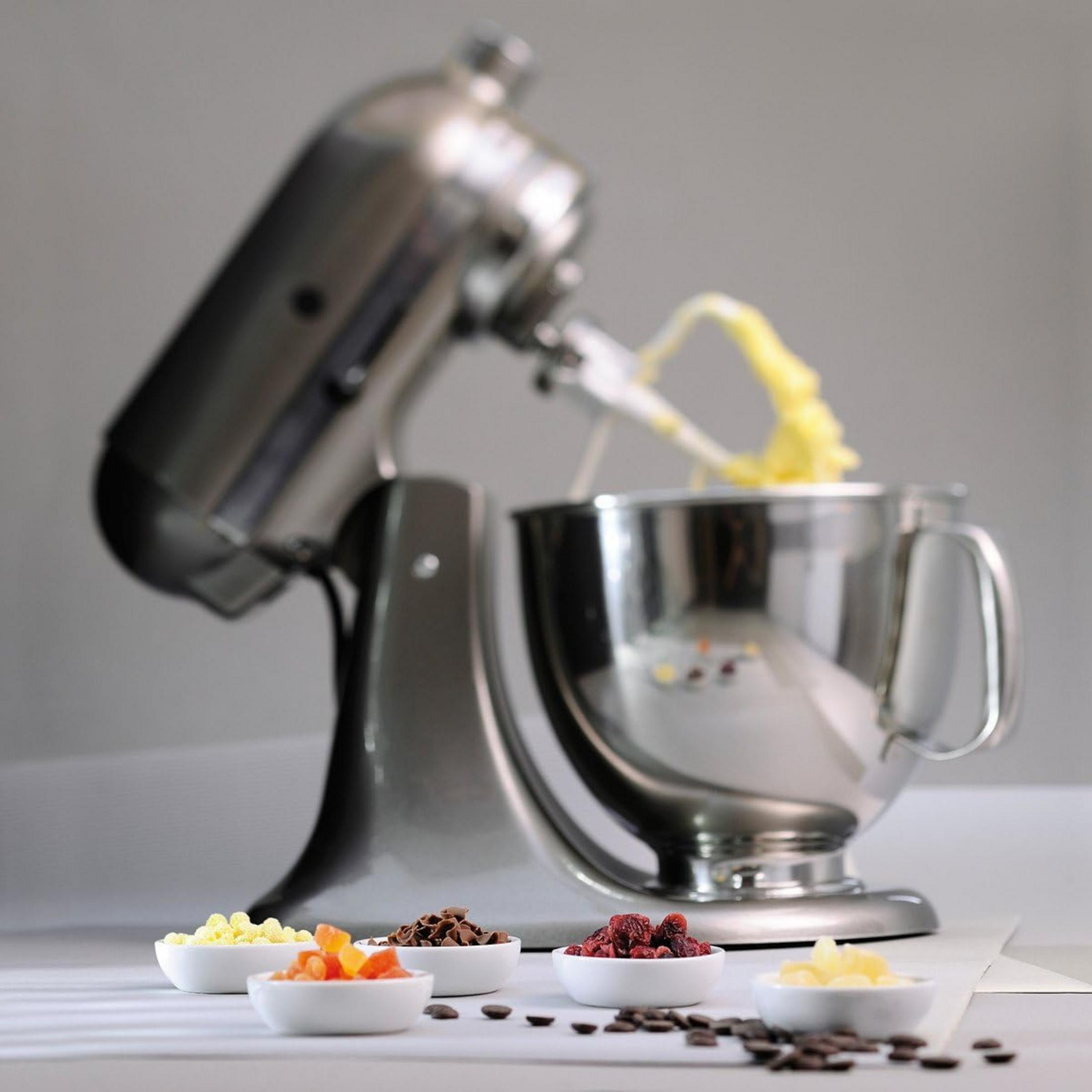 Eine Küchenmaschine mit einer Schüssel gelbem Teig und kleinen Schüsseln mit Zutaten.