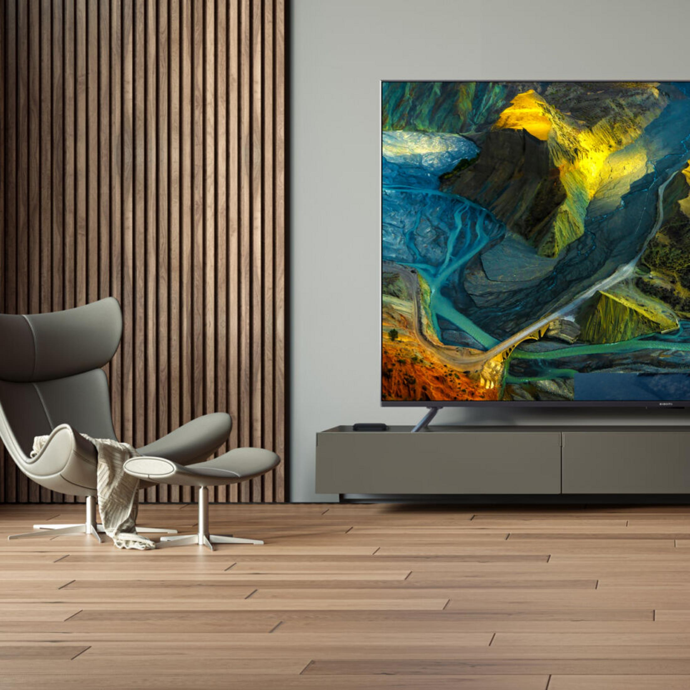 Un sillón moderno junto a un televisor que muestra una vista aérea del paisaje.