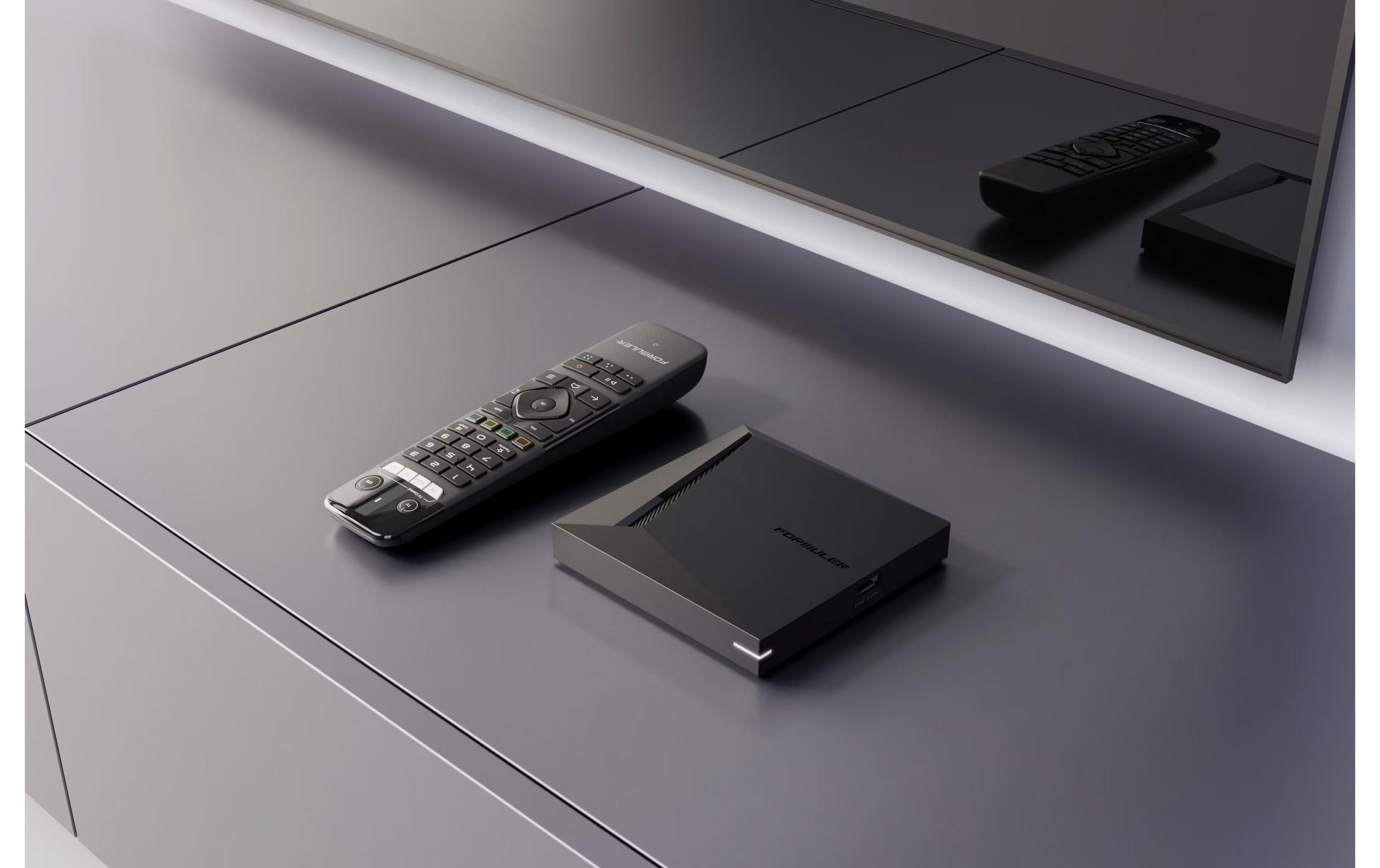 Un telecomando nero e un set-top box nero sono su un tavolo scuro.