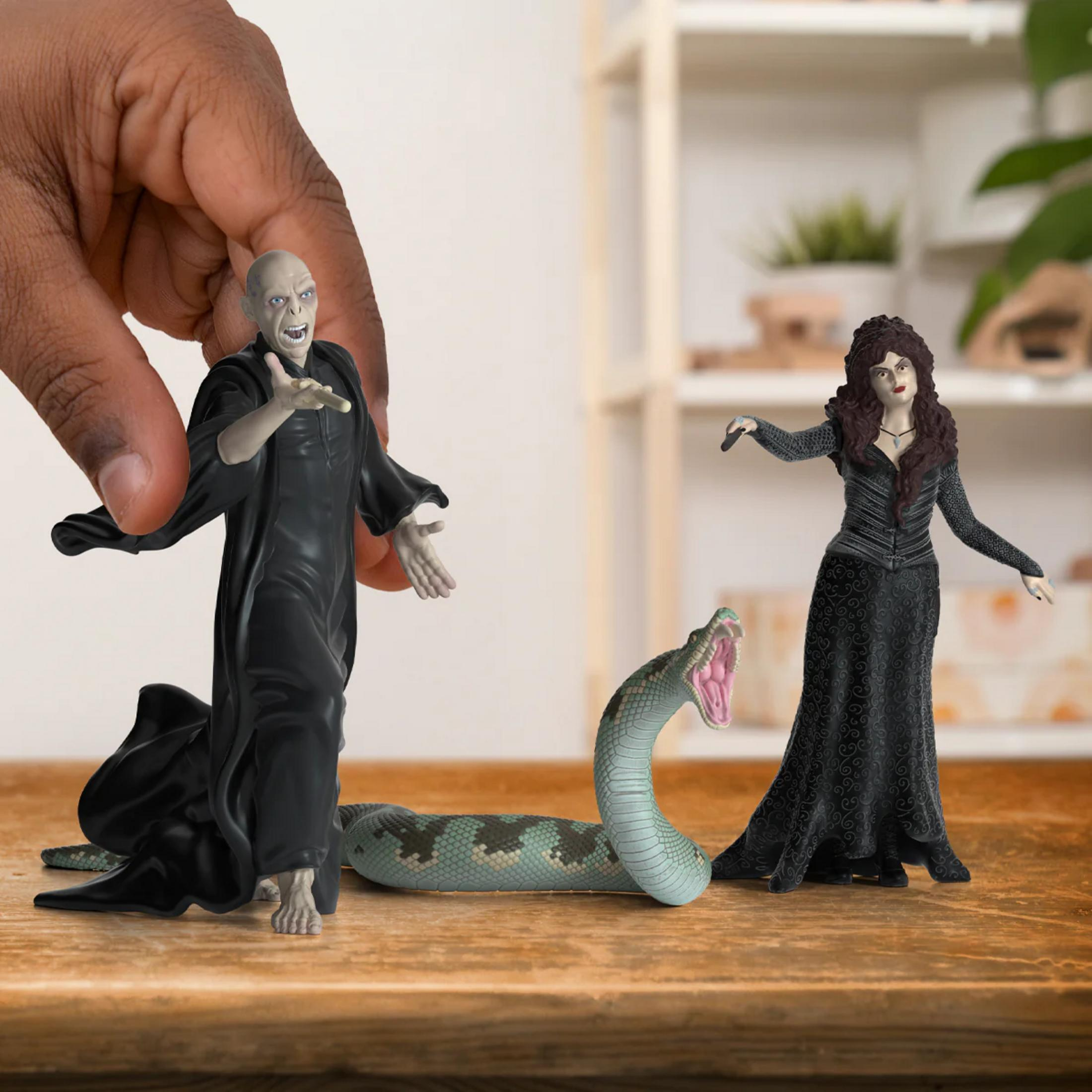 Una mano tiene una figura di Voldemort, accanto a un serpente e Bellatrix Lestrange.