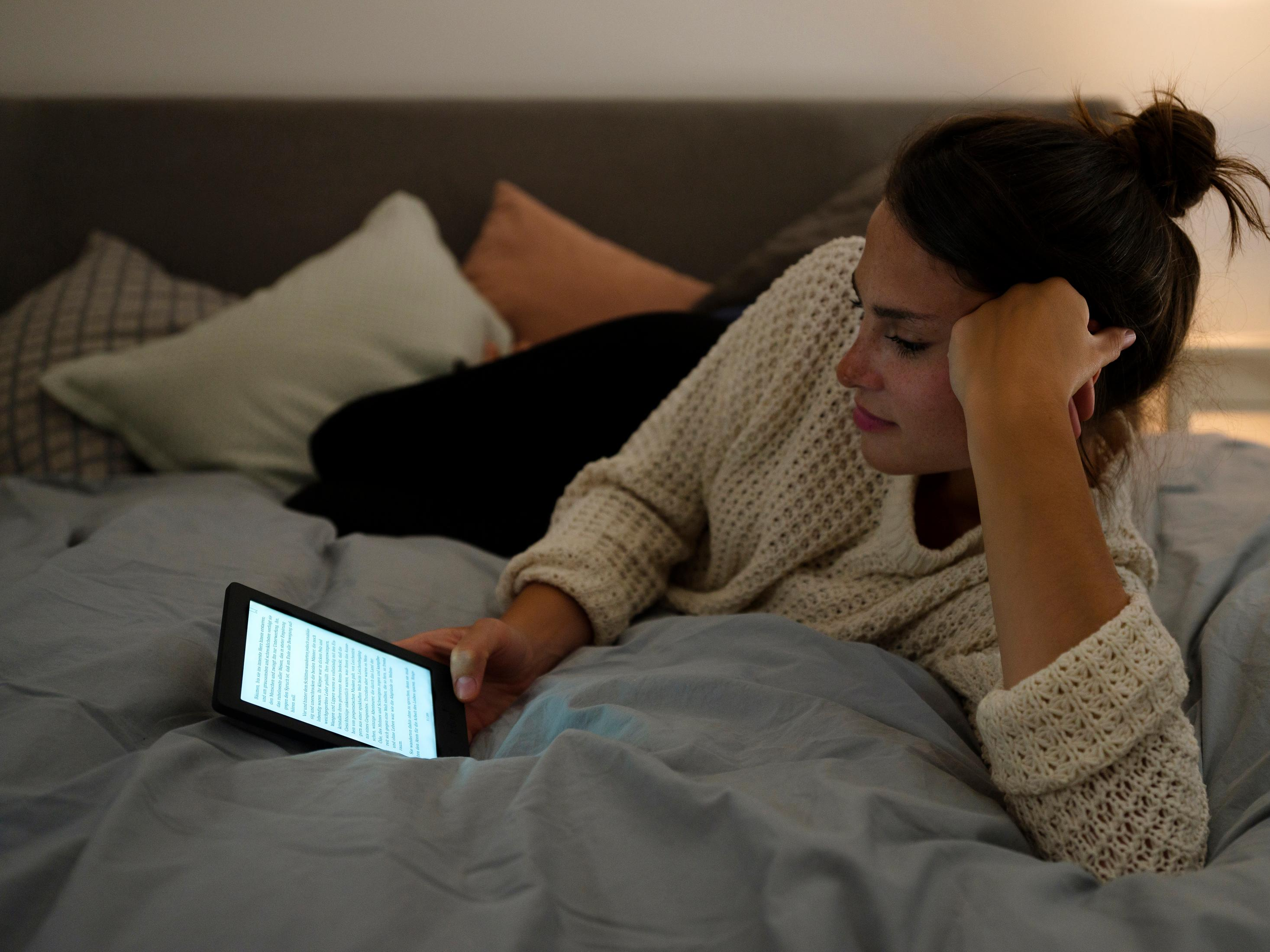 Eine junge Frau liegt im Bett und liest auf einem E-Reader.