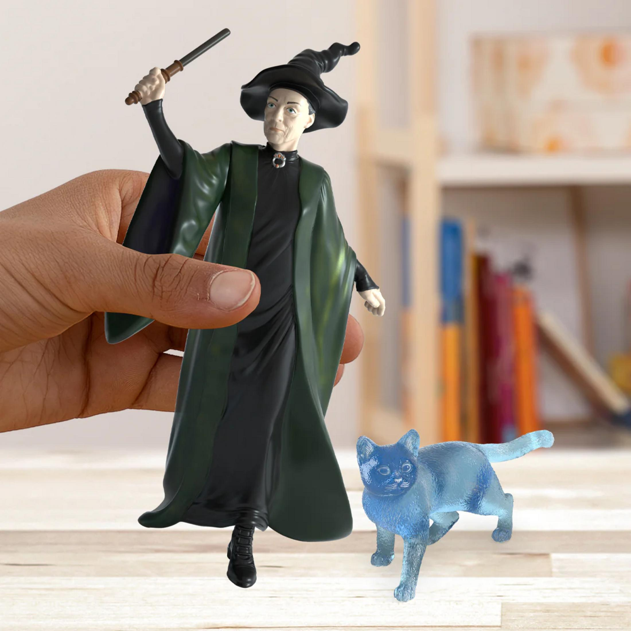 Una mano tiene una statuetta di strega con bacchetta accanto a una scultura di gatto blu.