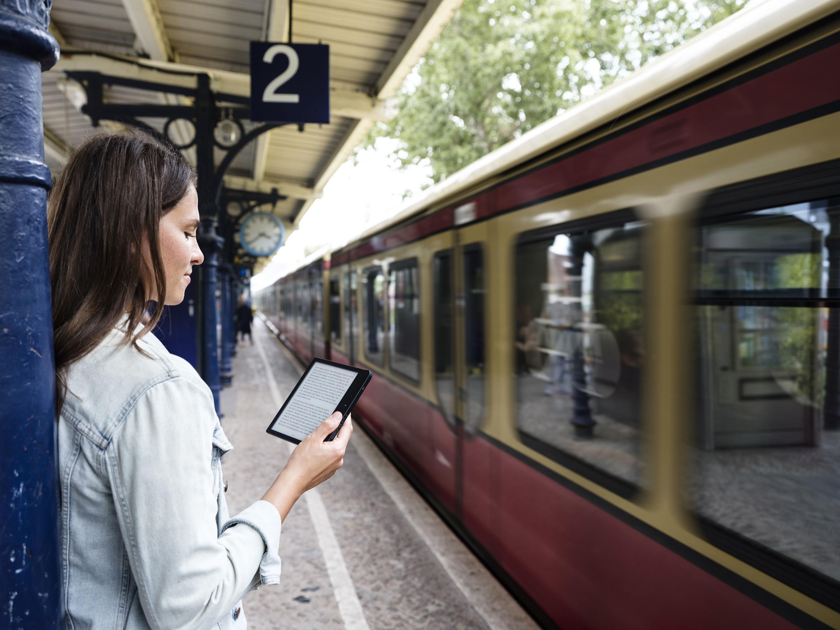 Donna legge e-reader sulla banchina accanto a un treno.