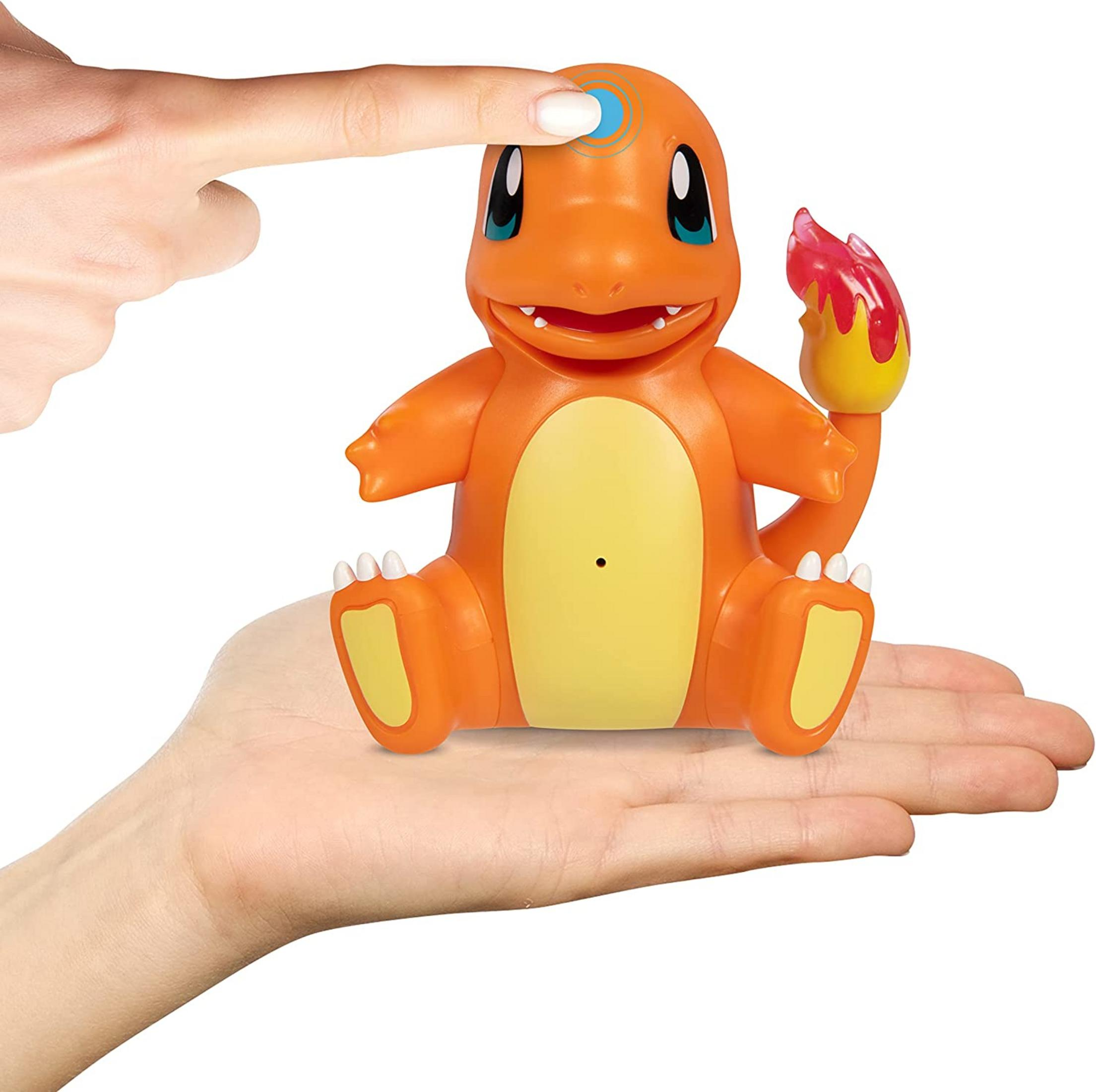Ein Finger drückt auf den Kopf einer orangen Charmander-Figur, die auf einer Hand sitzt.