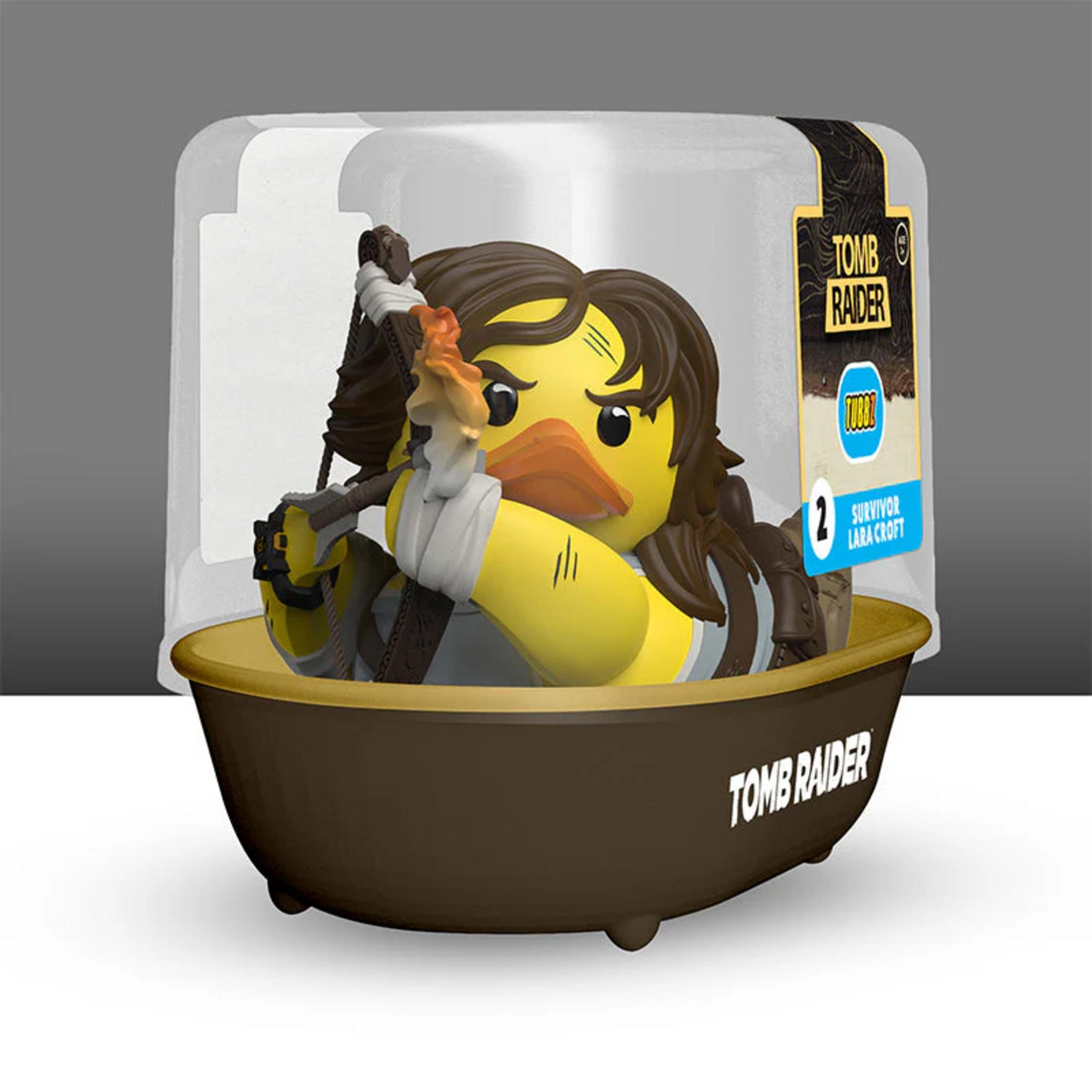 Lara Croft als gelbe Ente mit Fackel in einer braunen Wanne, verpackt in einer Plastikbox.