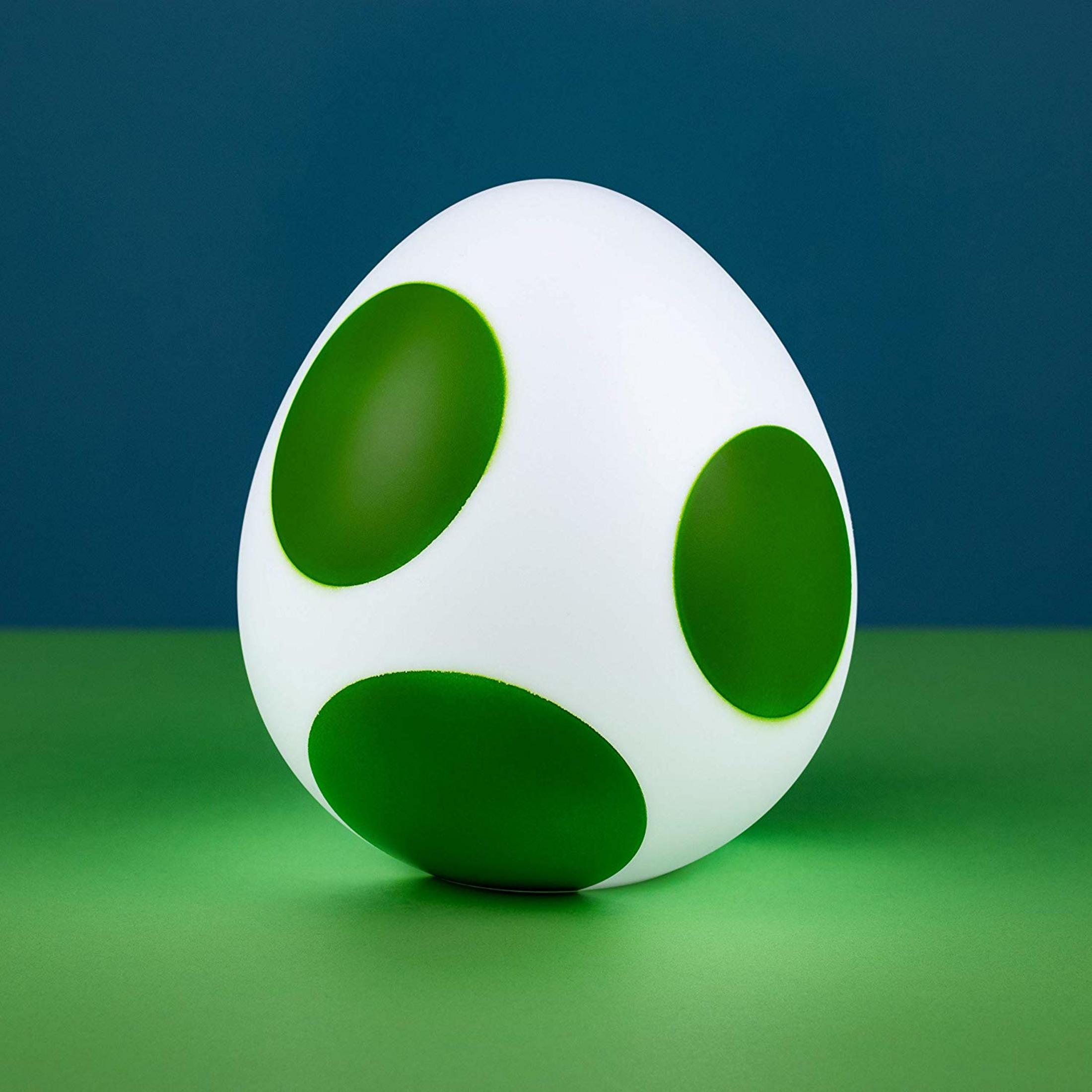 Un œuf blanc à pois verts repose sur une surface verte devant un fond bleu foncé.