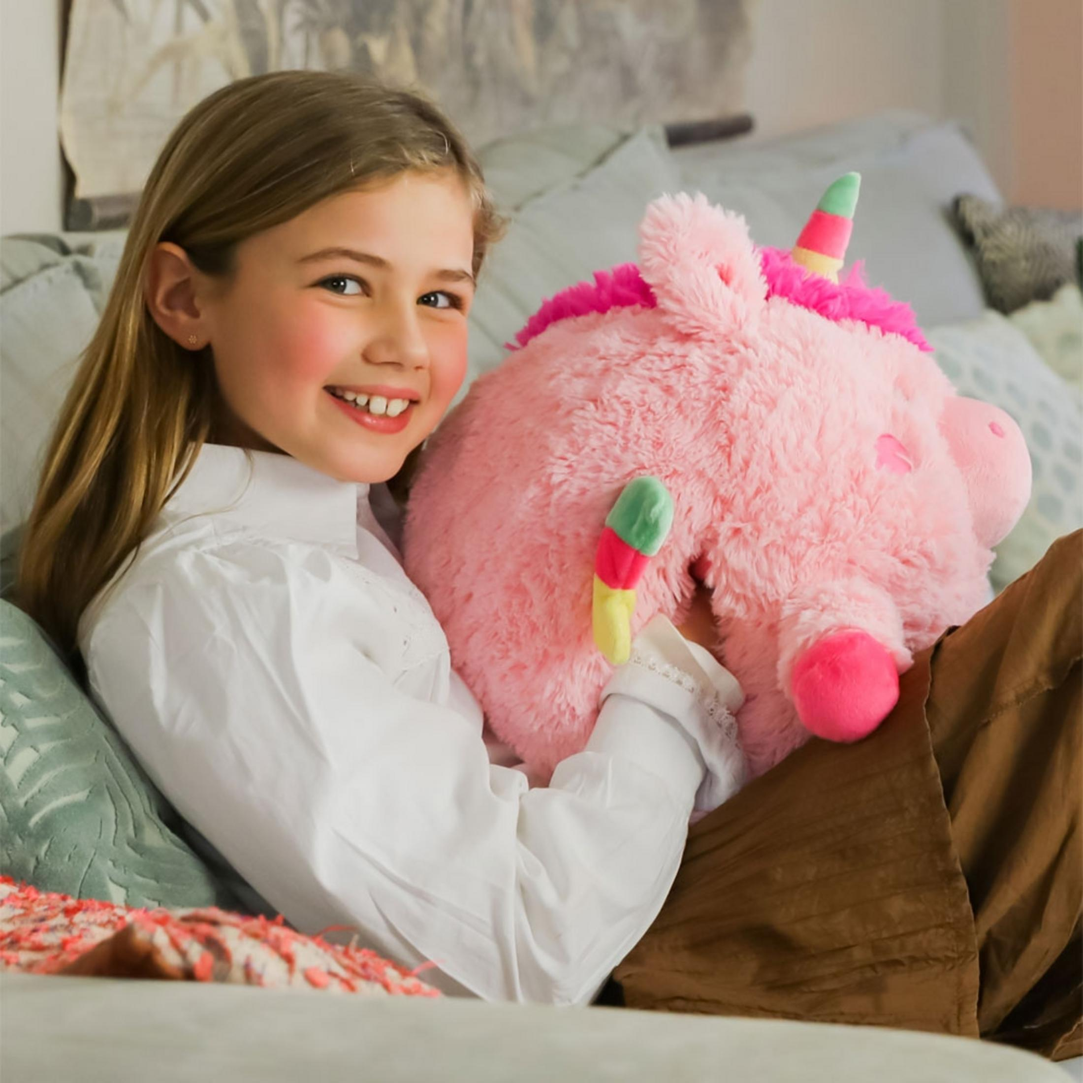 Ein Mädchen mit blonde Haaren hält ein rosa Einhorn-Plüschtier, sitzt auf einem Sofa.