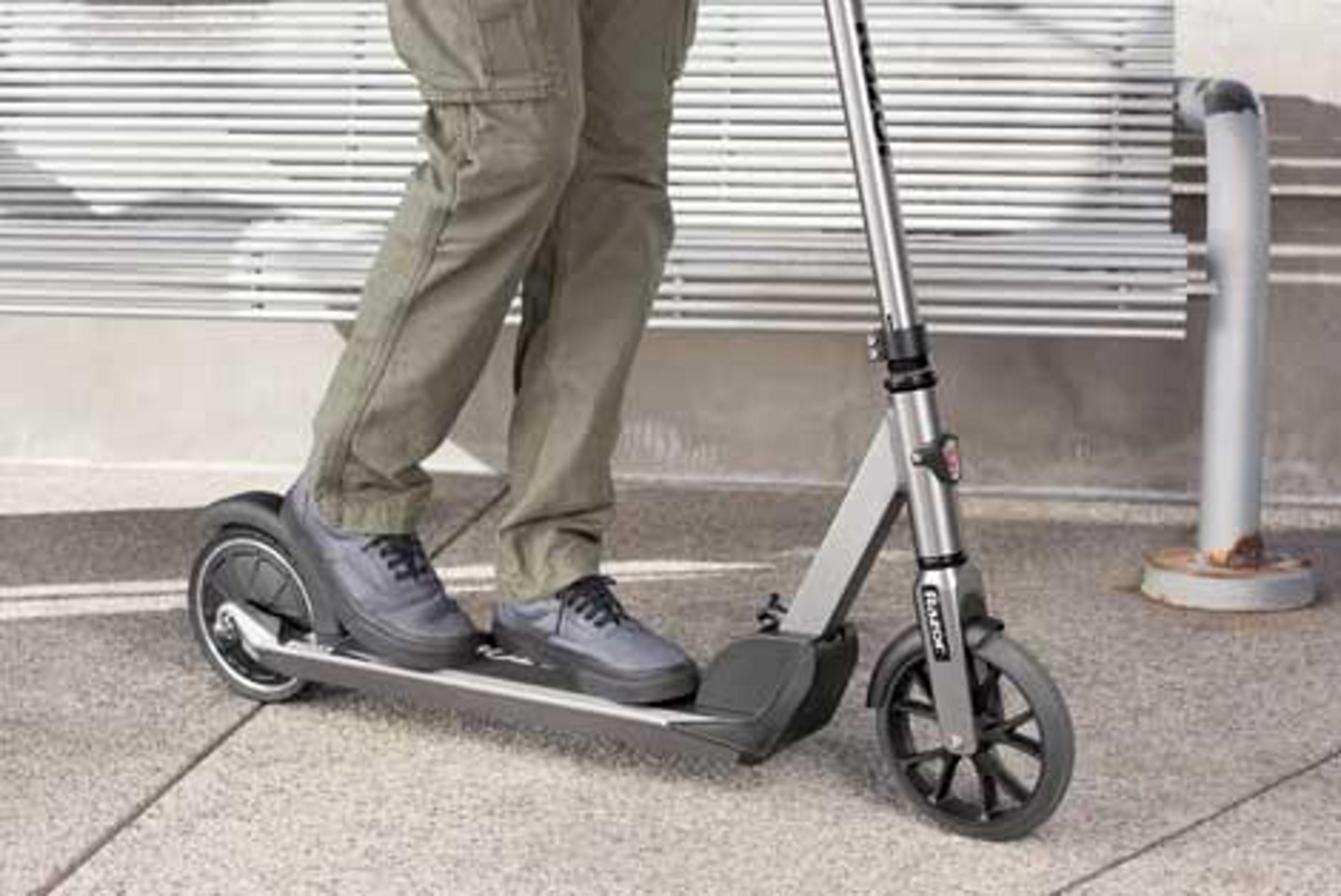Person stands on a silver e-scooter wearing black shoes and cargo pants.