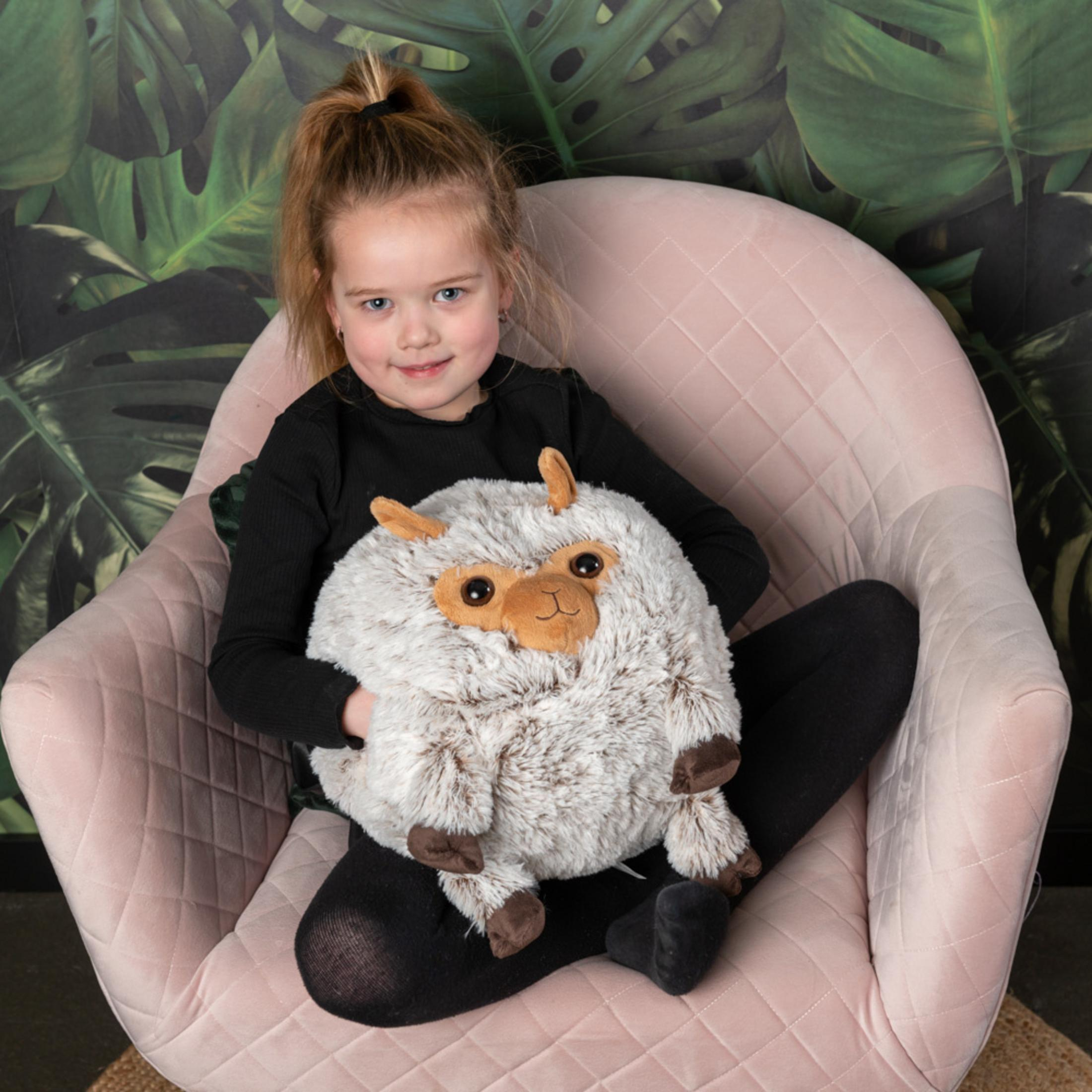 Ein kleines Mädchen sitzt in einem rosa Sessel und hält ein flauschiges Stofftier.