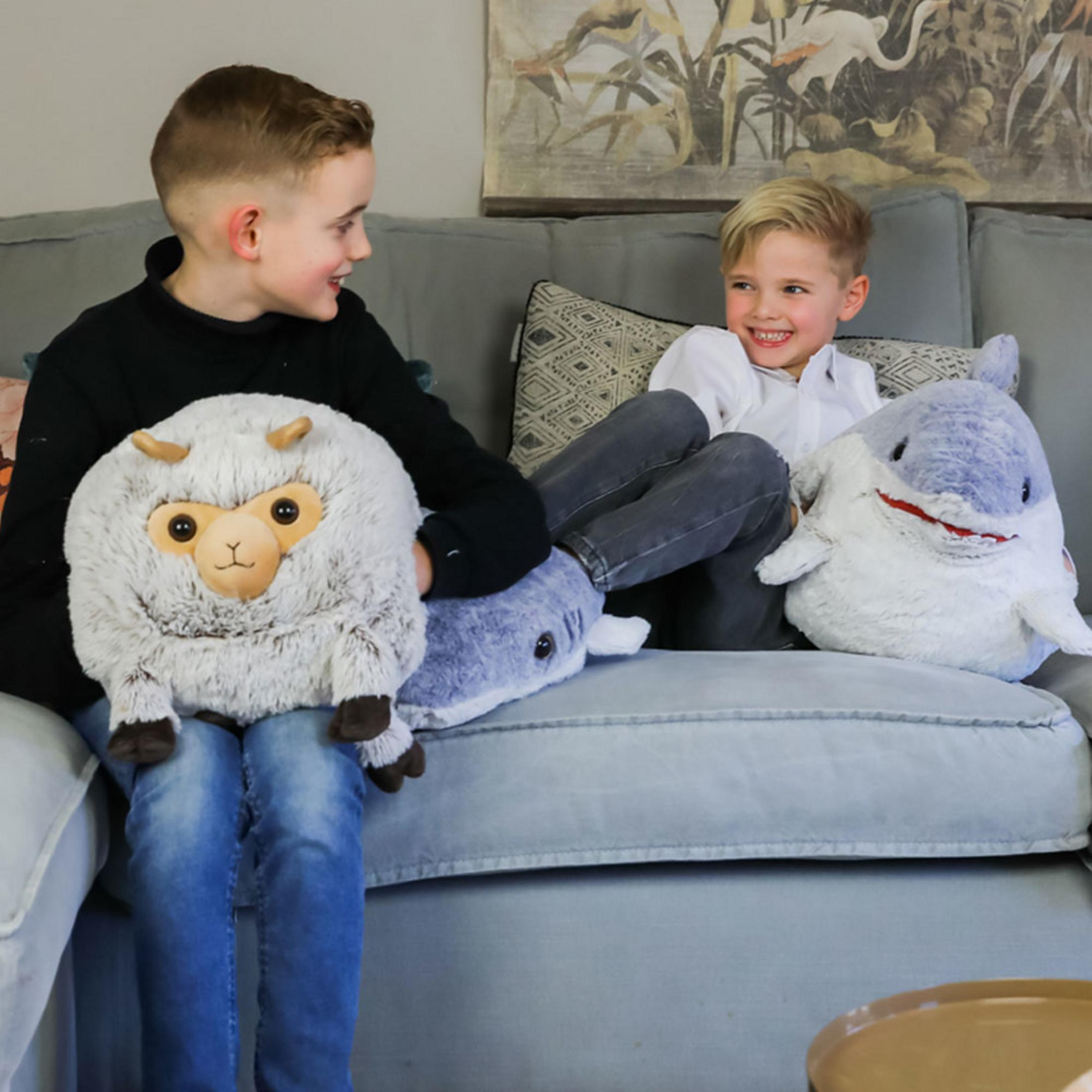 Zwei Jungen sitzen auf einem Sofa mit Plüschtieren: einem Schaf und zwei Haien.