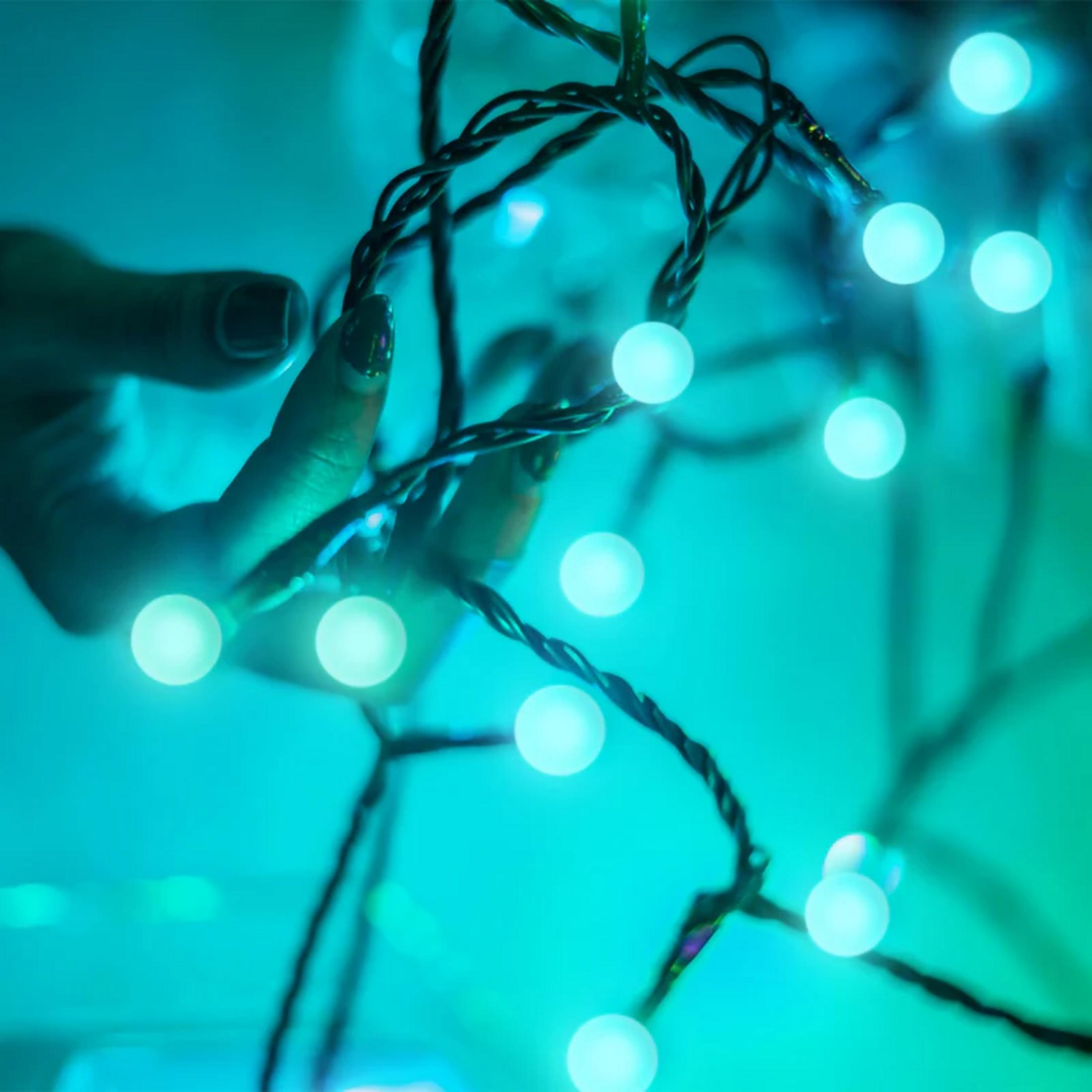 Dłoń trzyma sznur niebieskich światełek na turkusowym tle.