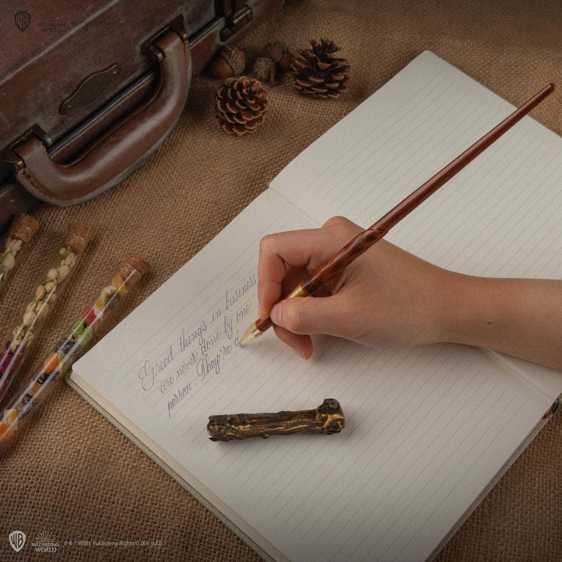 Une main écrit dans un carnet avec une plume. De petits flacons sont à côté.