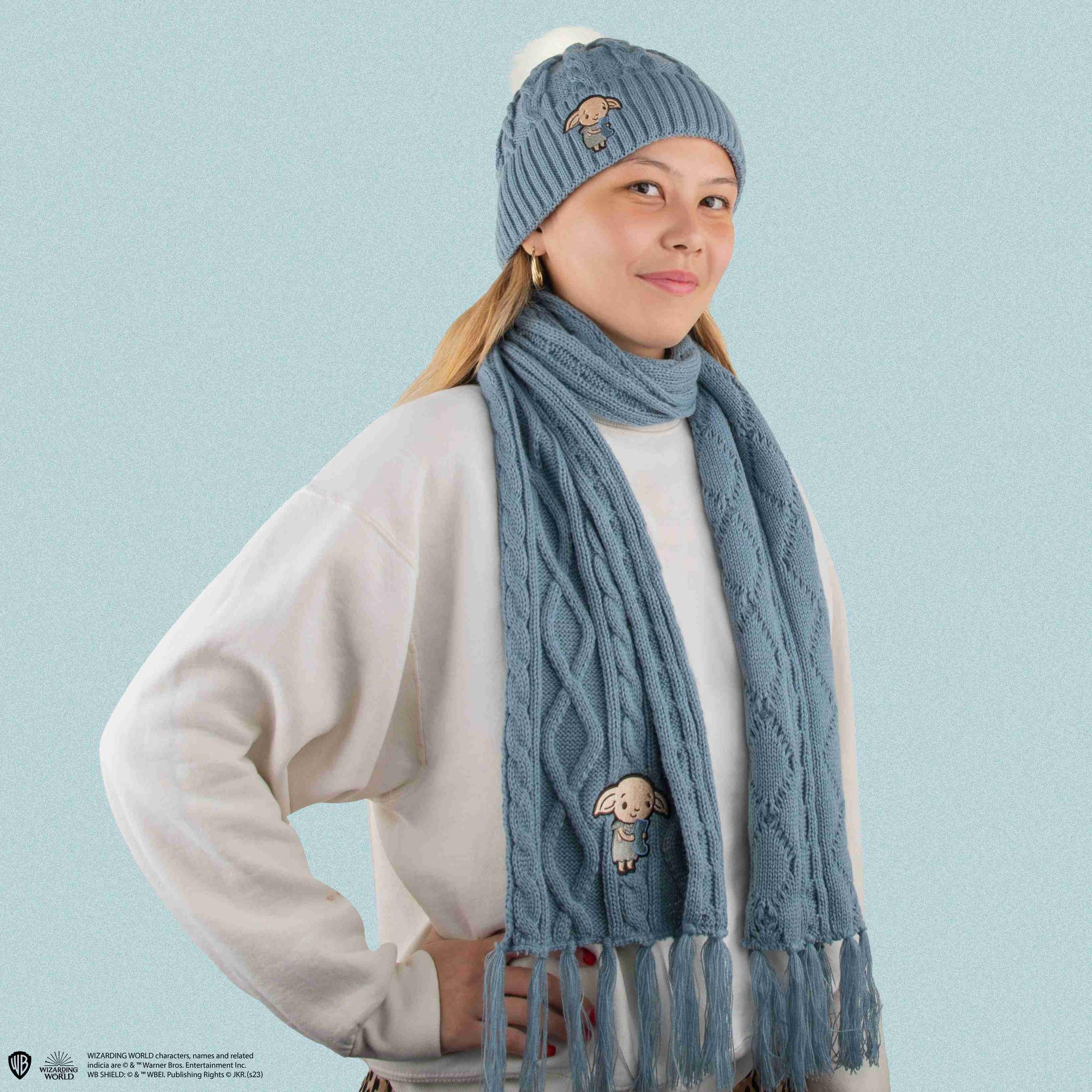 Eine Frau trägt eine blaue Strickmütze und einen Schal mit Dobby-Motiv.