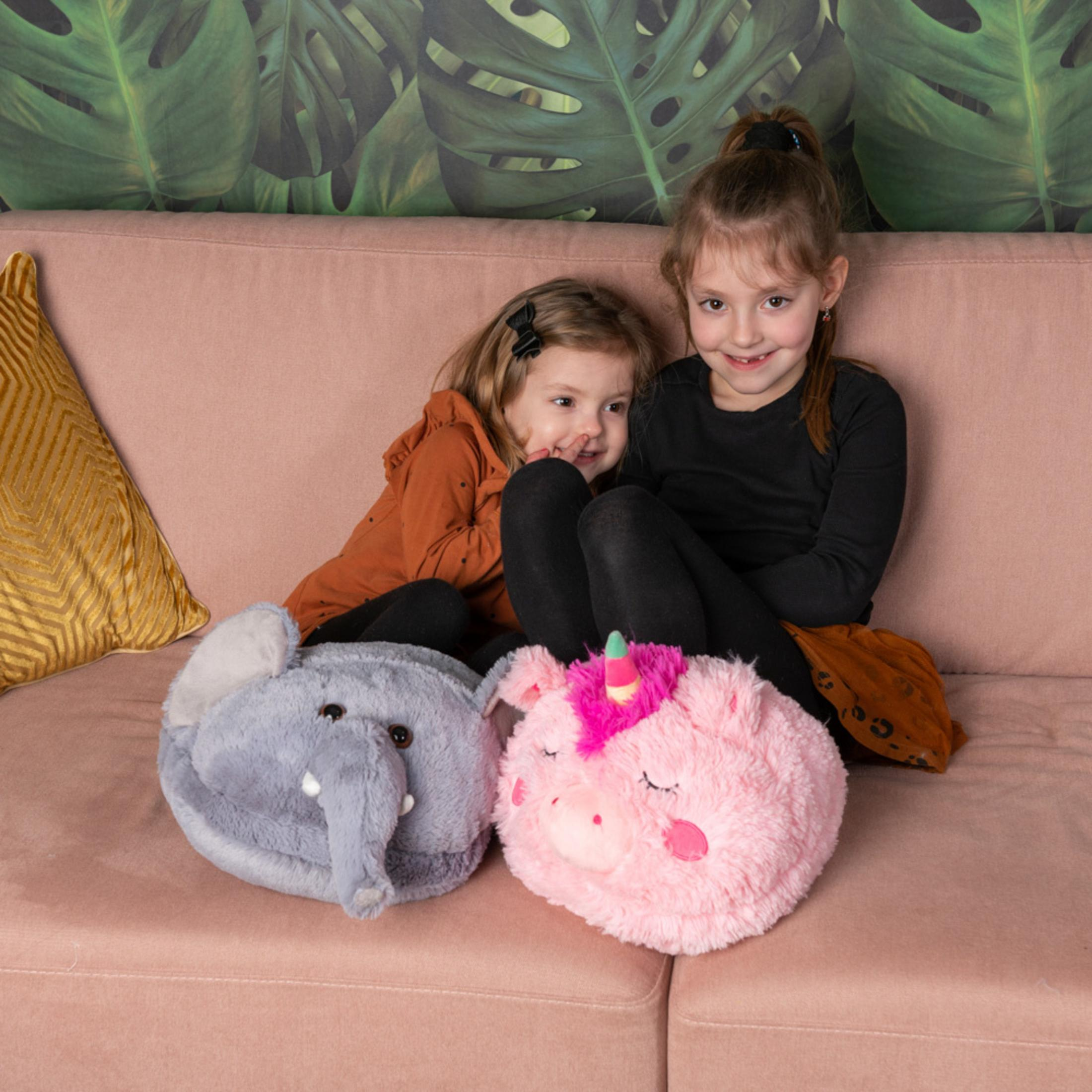 Zwei Mädchen sitzen auf einer rosafarbenen Couch neben Plüschtieren.