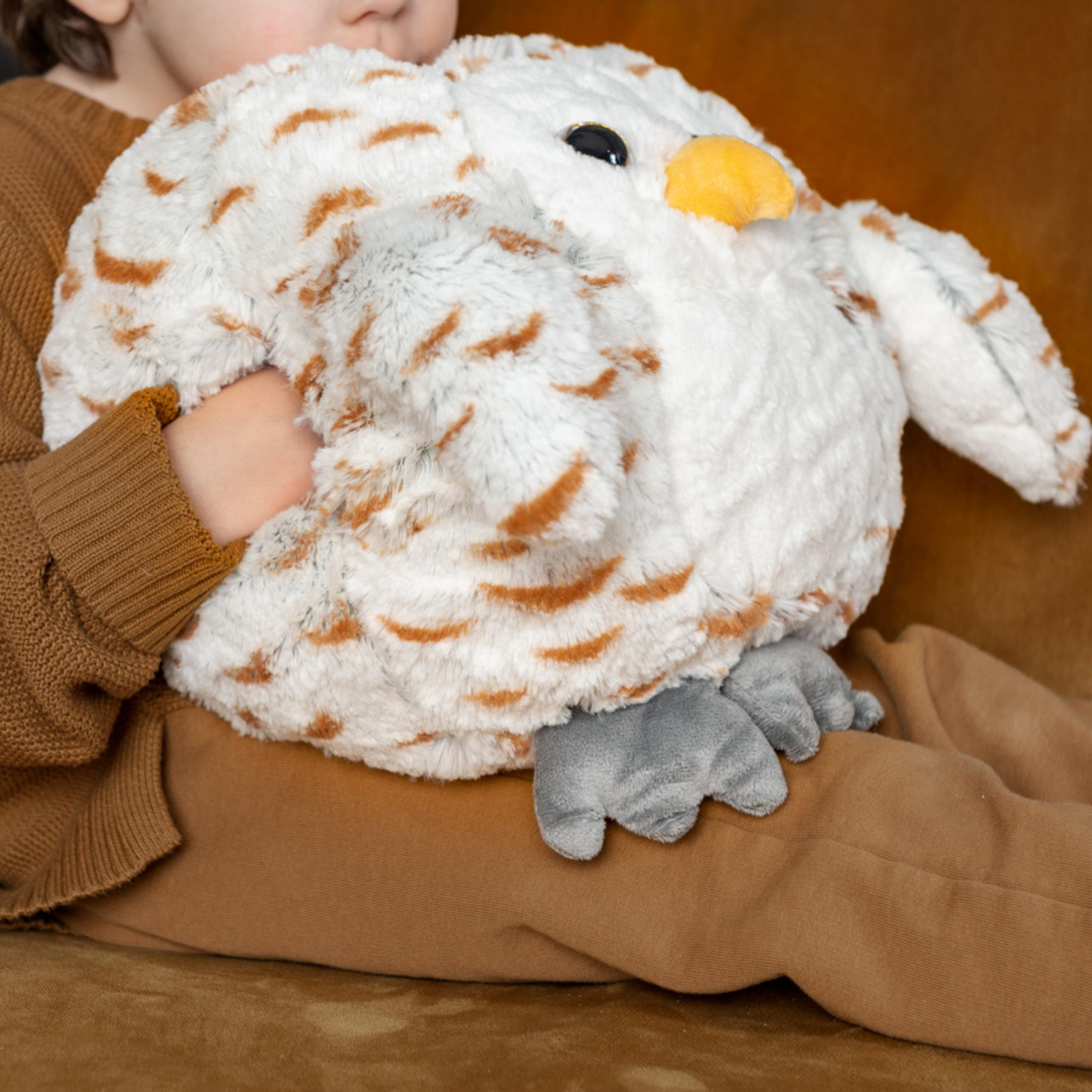 Ein Kind hält eine weiche, weiße Eulenpuppe mit braunen Flecken.