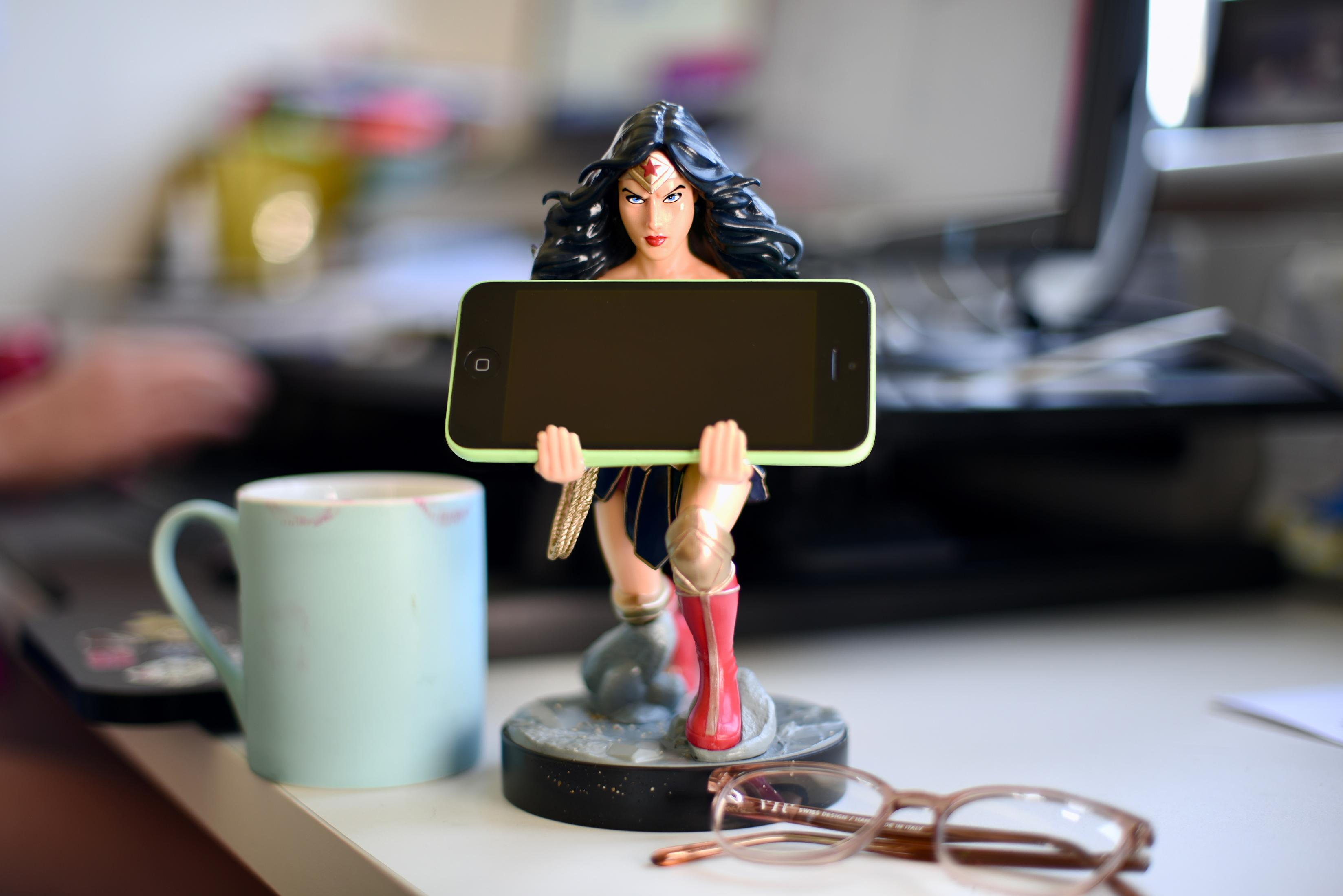 Statua di Wonder Woman tiene uno smartphone. Accanto, una tazza e occhiali.