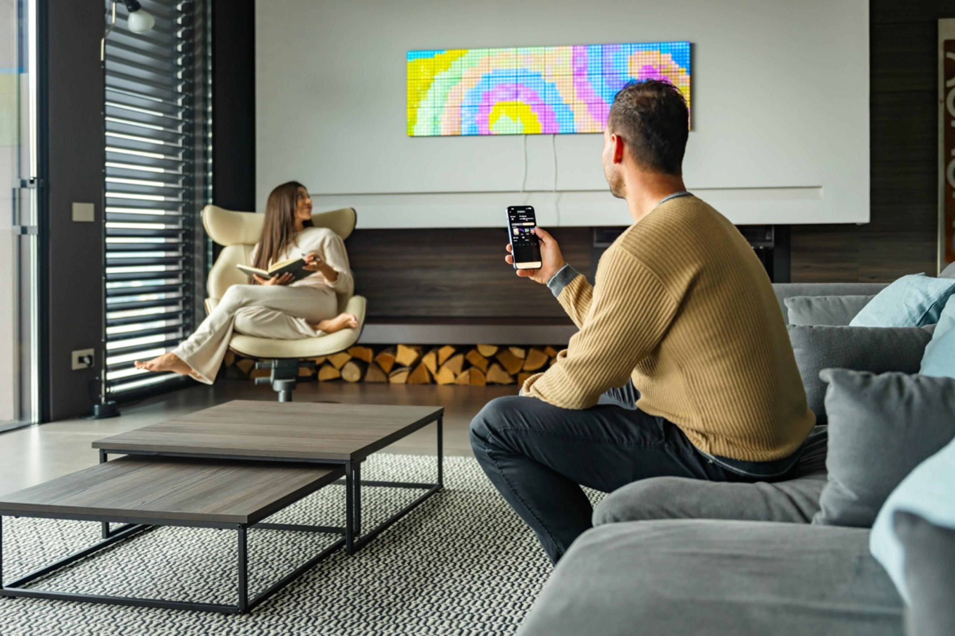 Mężczyzna z telefonem na kanapie, kobieta czyta książkę, kolorowa sztuka na ścianie.