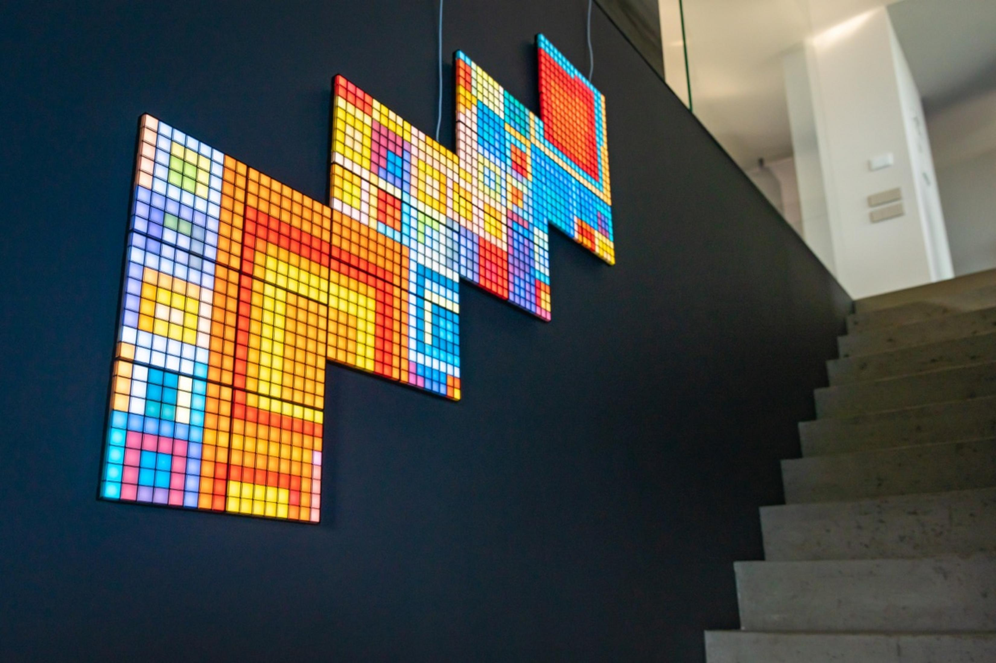 Kolorowe instalacje pixel art na ciemnej ścianie nad kamiennymi schodami.