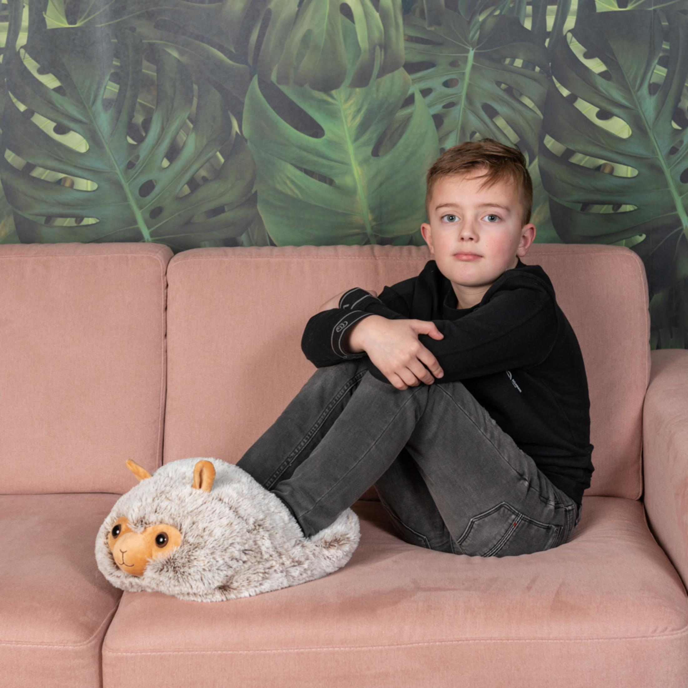 Ein Junge sitzt auf einer rosa Couch mit einem Lama-Hausschuh.