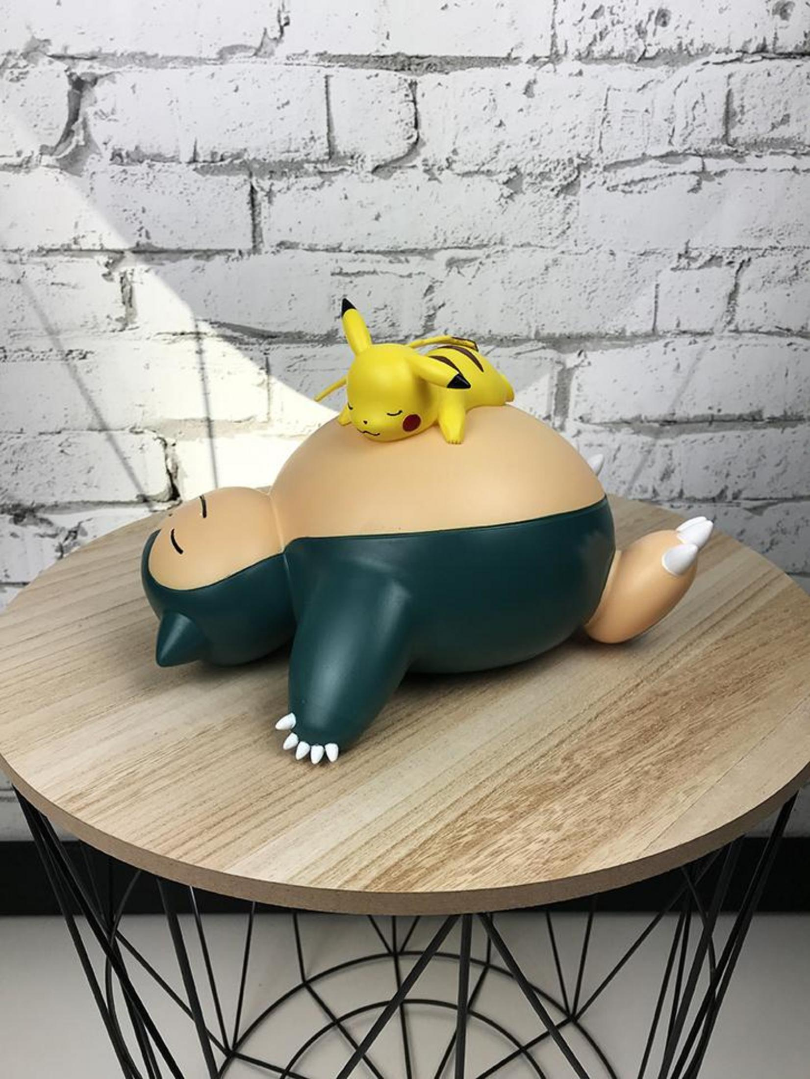 Pikachu riposa su uno Snorlax addormentato. Entrambe le figure sono su un tavolo di legno.