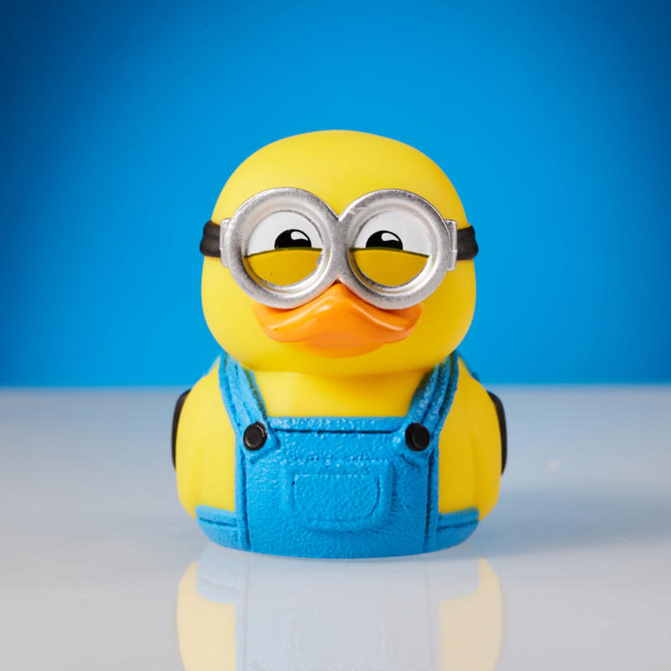 Gelbe Minion-Ente mit blauer Latzhose und Brille auf blauem Hintergrund.