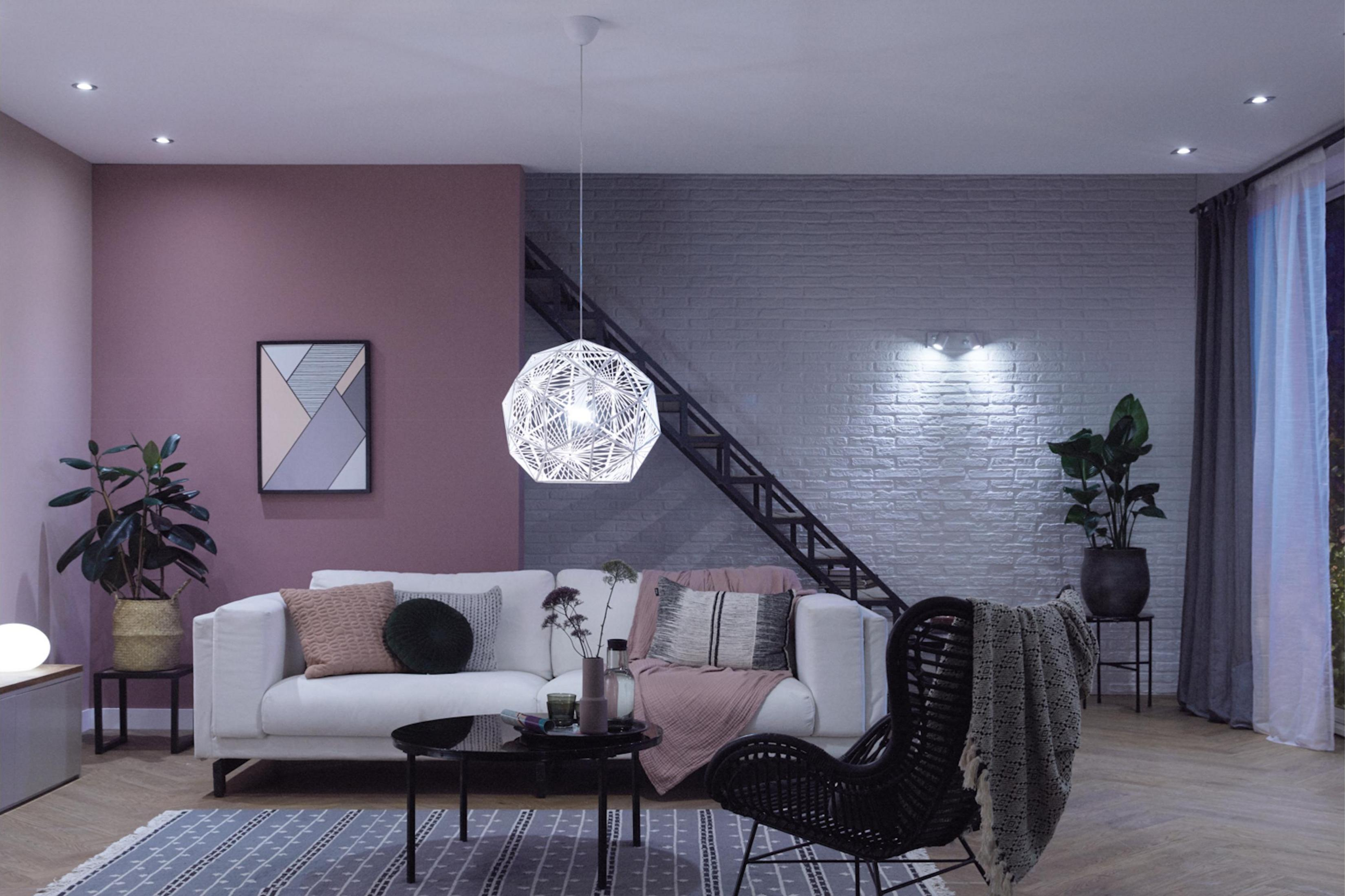 Stylowy salon z białą sofą, czarnym fotelem z rattanu i lampą wiszącą.