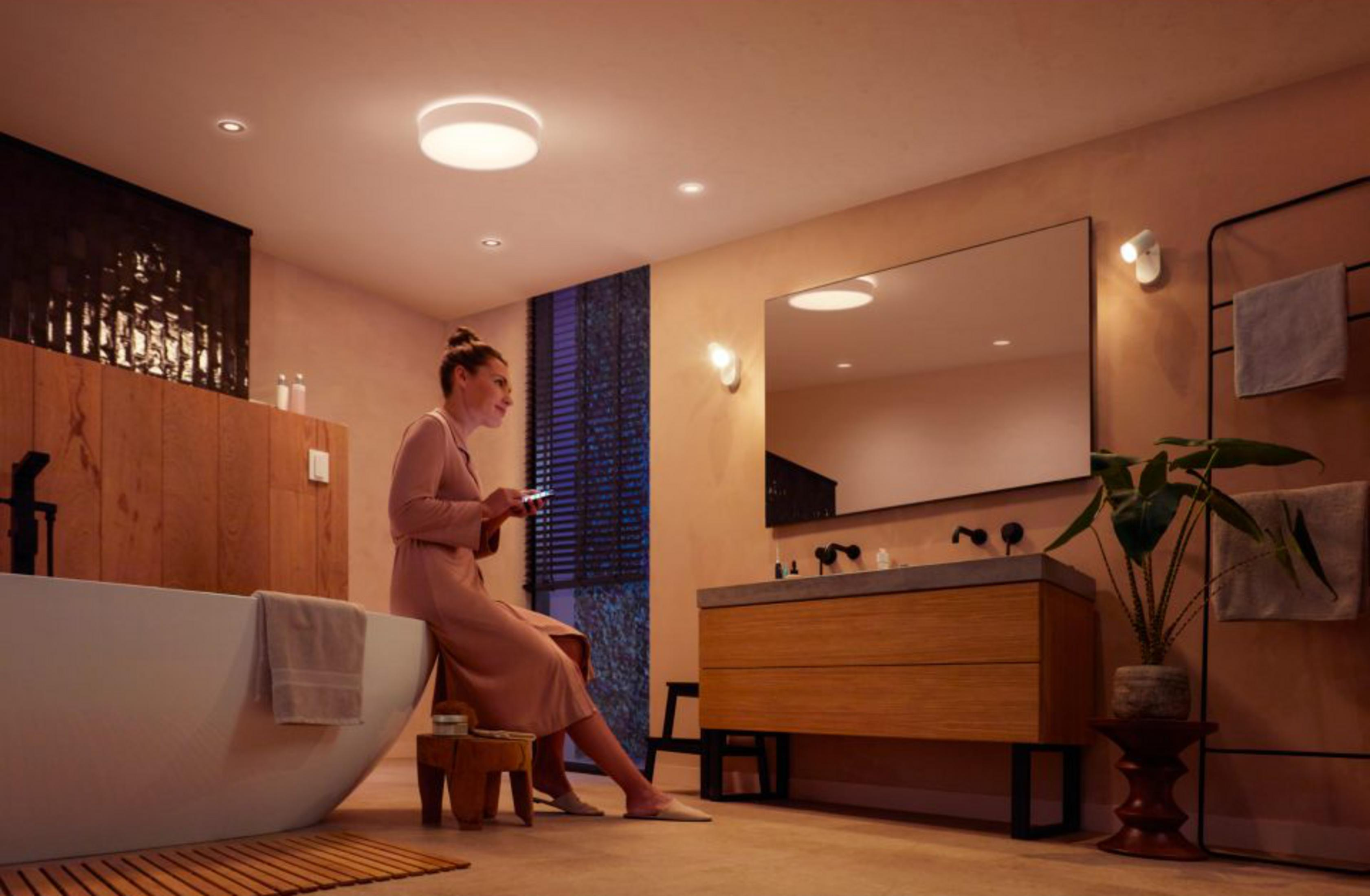 Una donna seduta su uno sgabello in un bagno usa il suo telefono.
