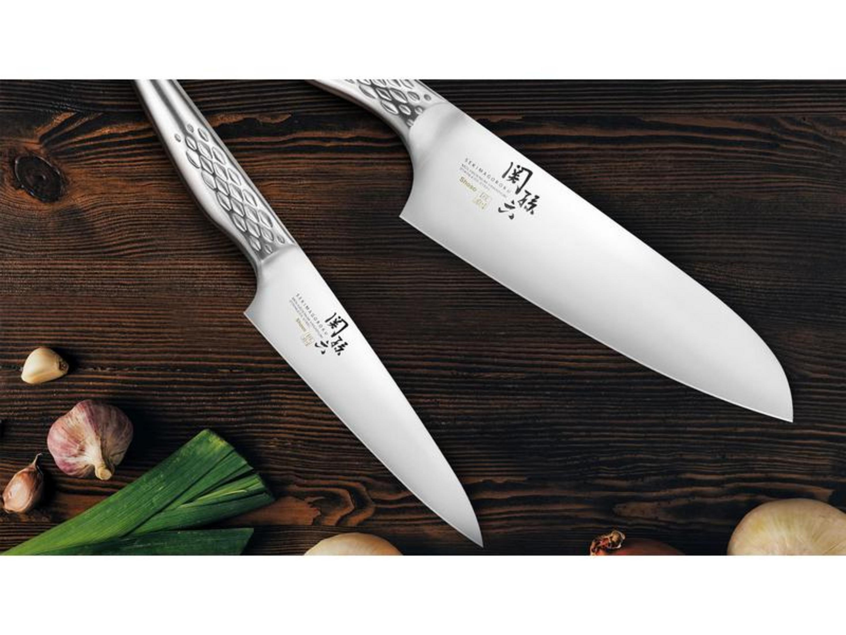 Zwei silberne Küchenmesser liegen auf einem Holztisch mit Knoblauch und Lauch.