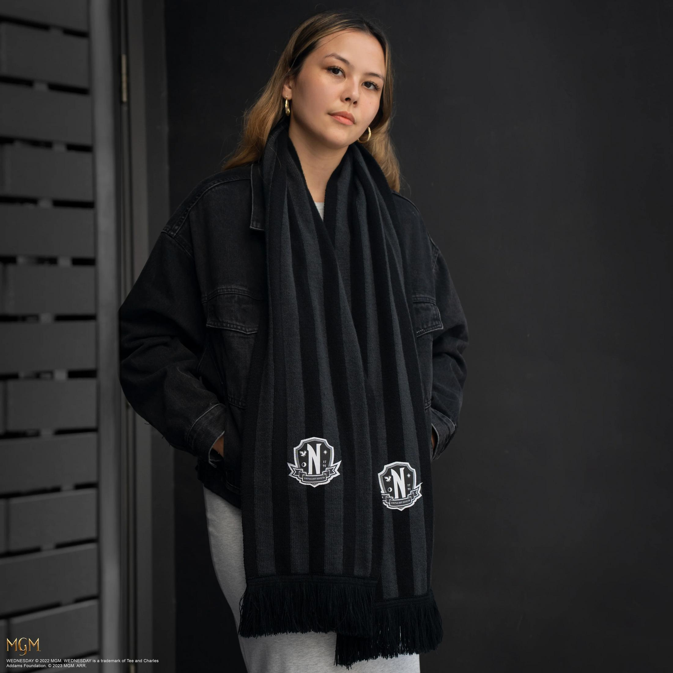 Eine Frau trägt einen gestreiften Schal mit N-Logos vor schwarzem Hintergrund.