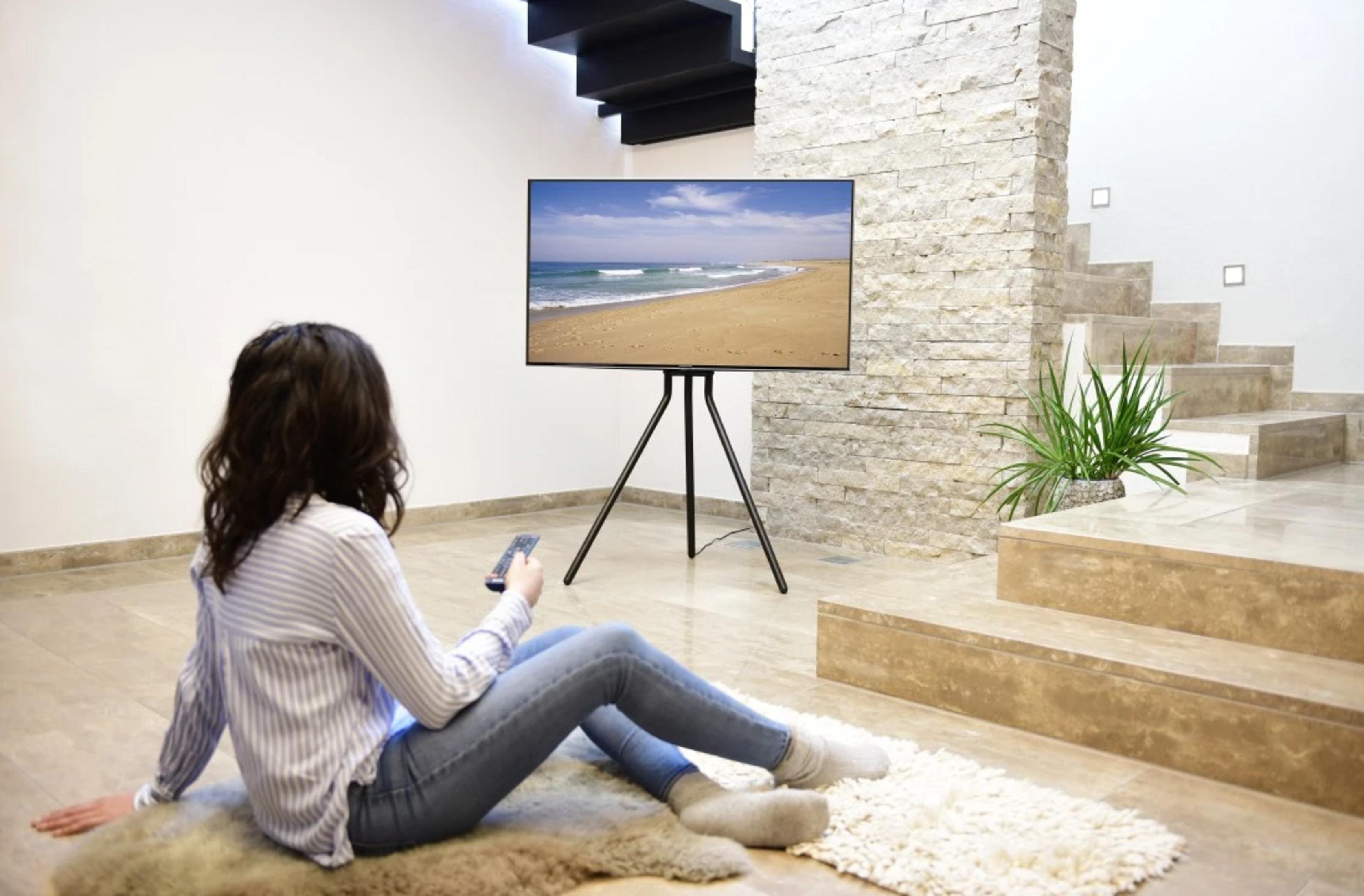 Kobieta siedzi na dywanie i ogląda telewizję. Schody w tle.