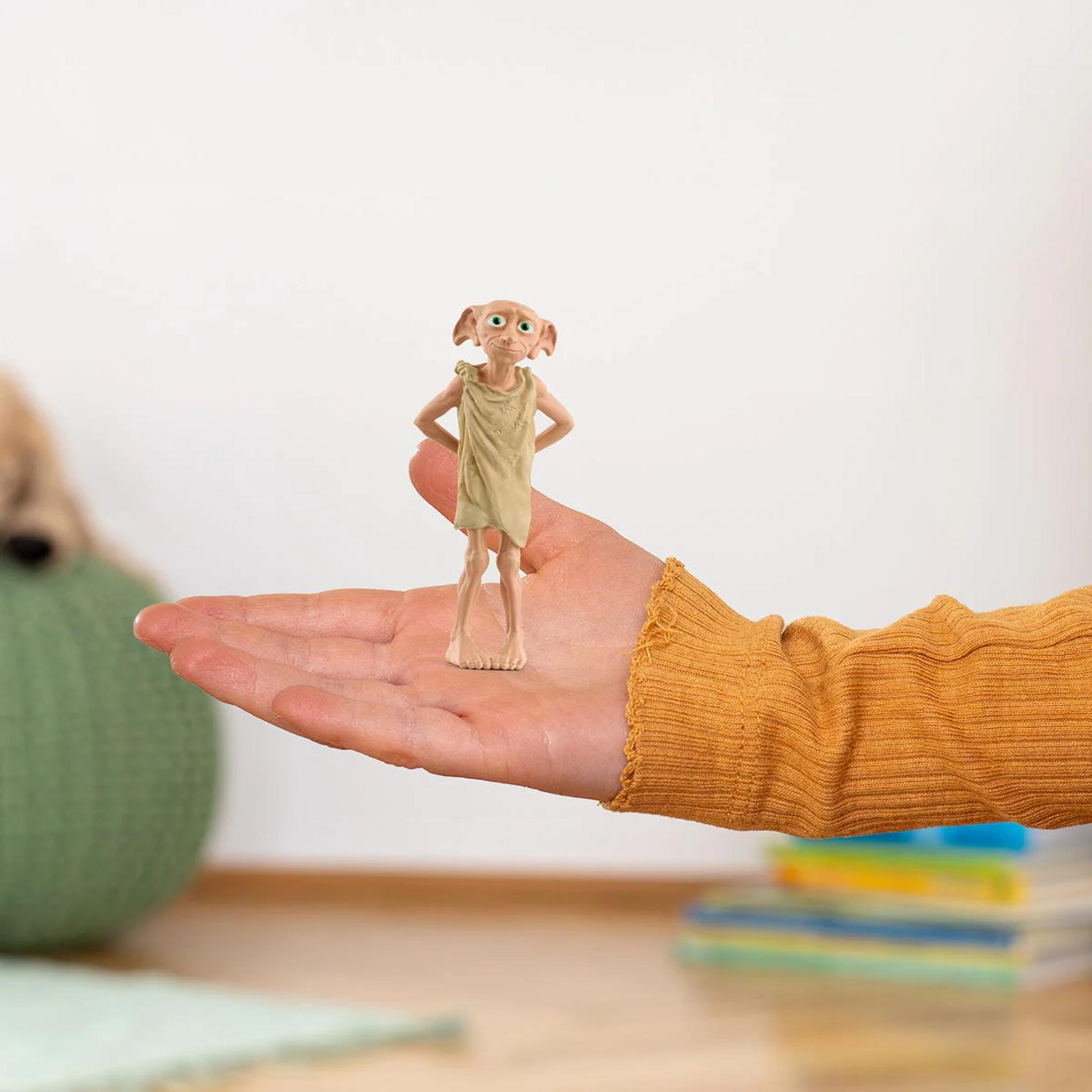 Eine kleine Dobby-Figur steht auf einer Hand. Im Hintergrund eine grüne Kugel.