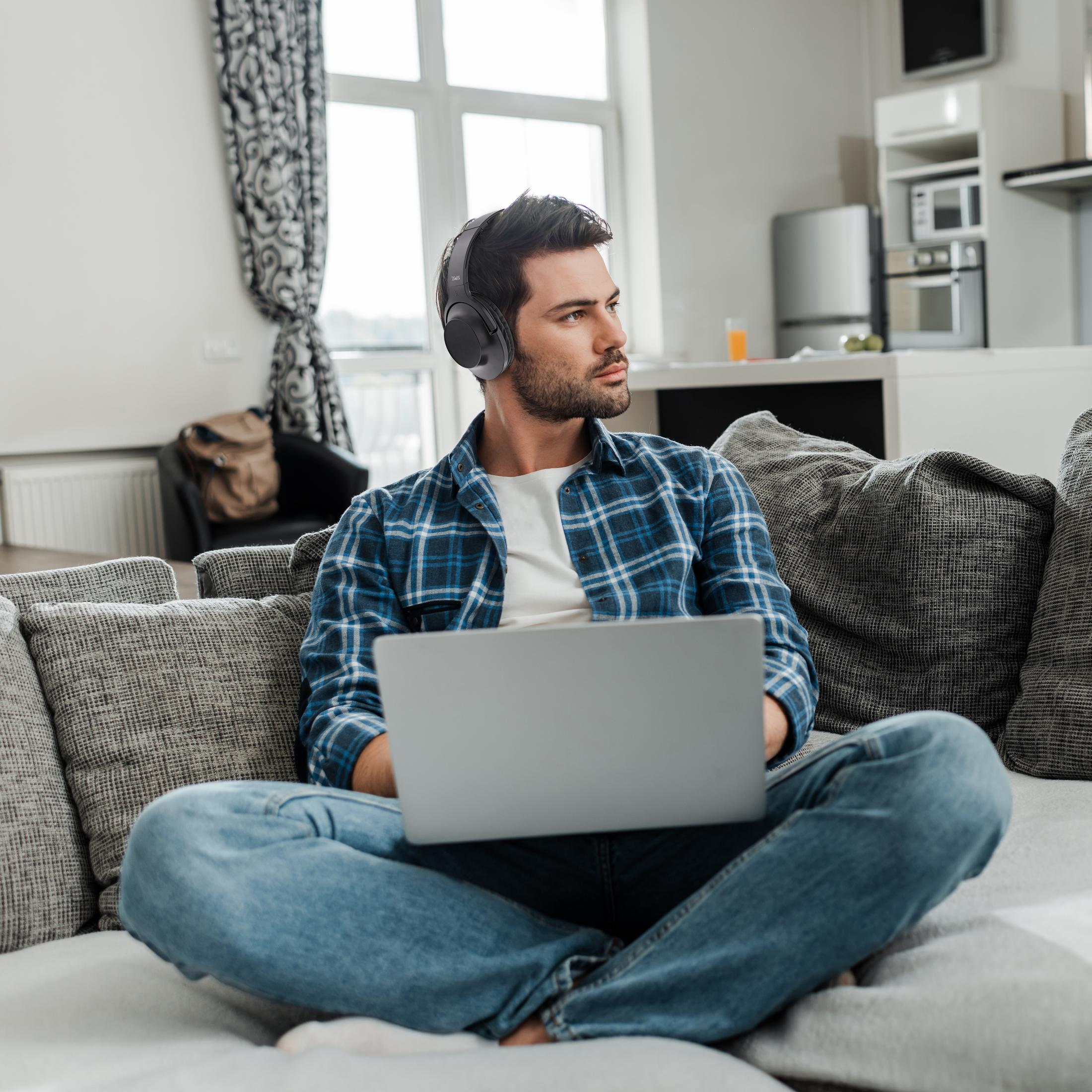 Un uomo con cuffie seduto su un divano usa un laptop.
