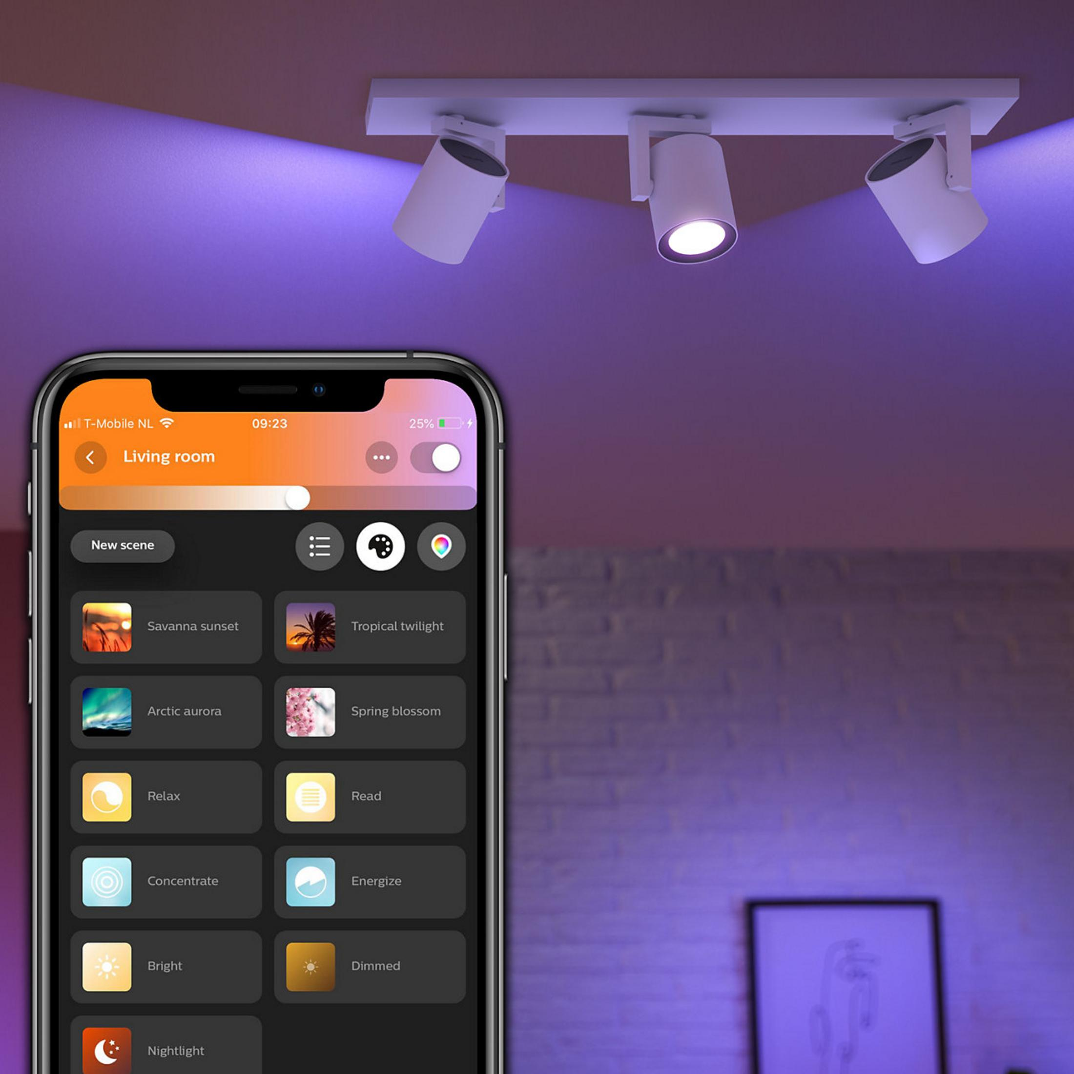 Uno smartphone mostra un'app di controllo luci con scene. Faretti a soffitto brillano di viola.