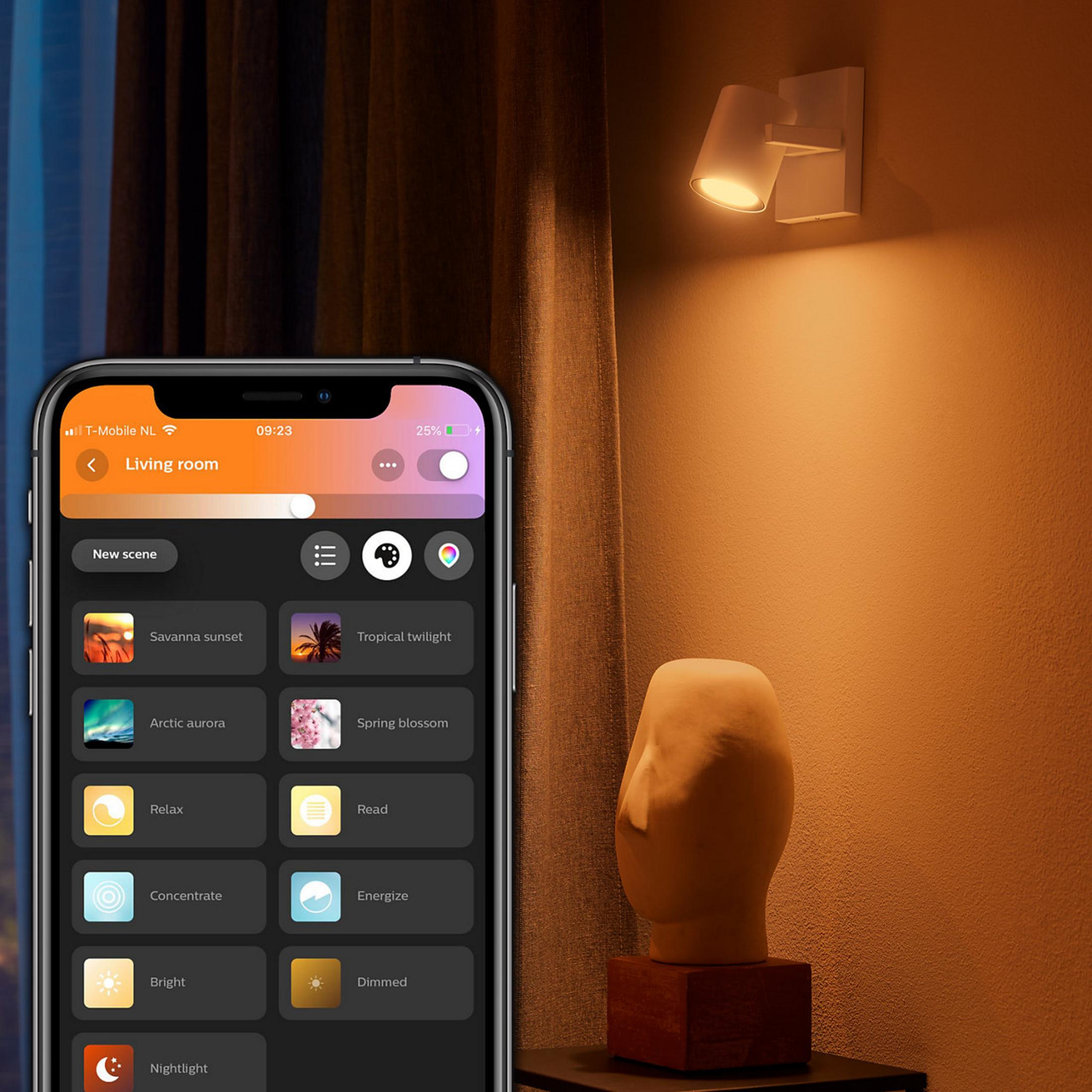 Uno smartphone mostra scene di illuminazione. Una lampada da parete illumina una stanza.