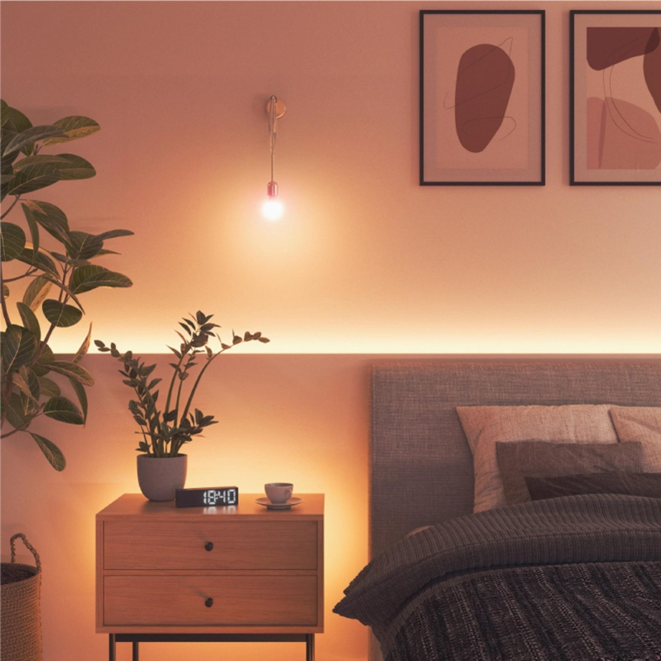 Un comodino con piante, orologio e tazza accanto a un letto.