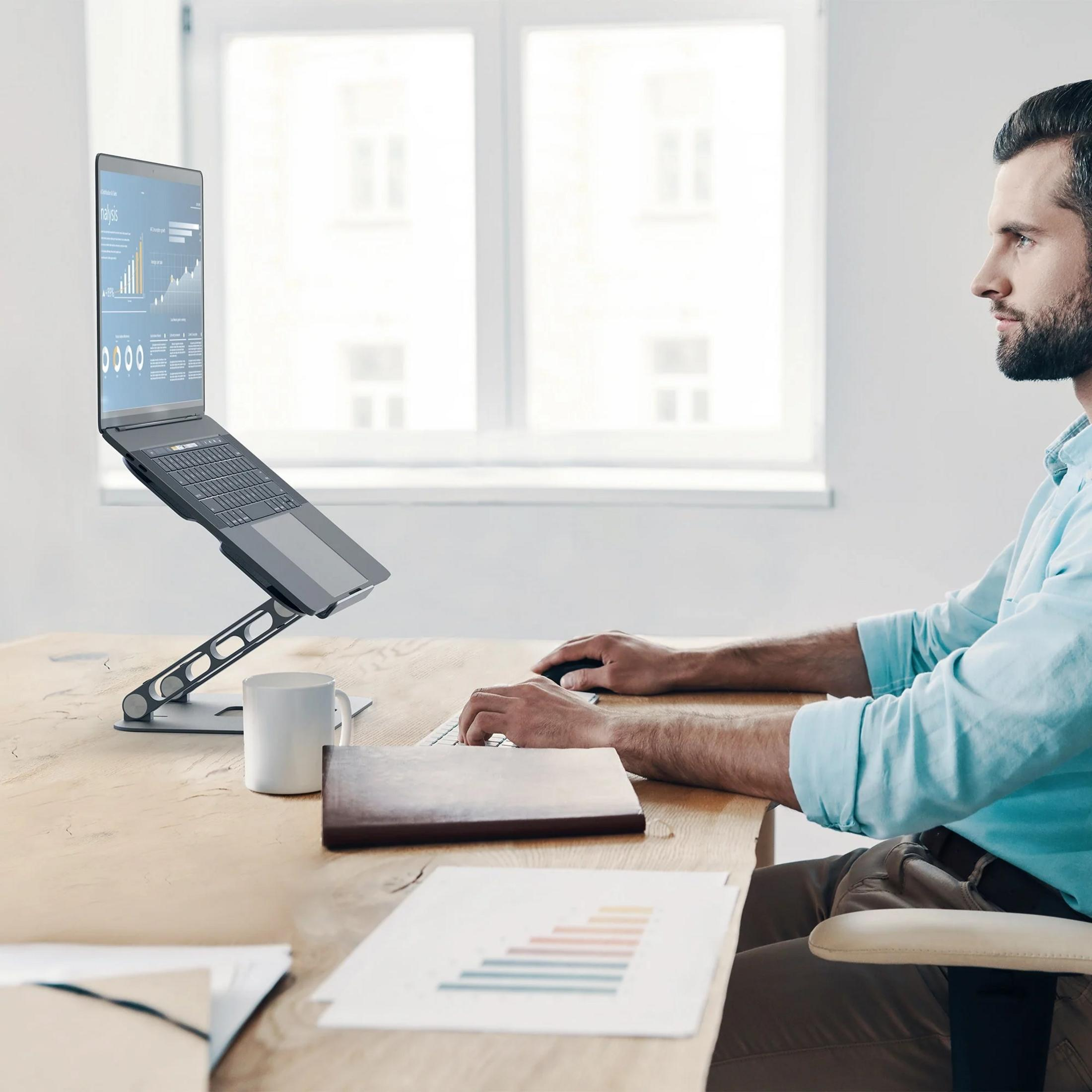 A man sits at a desk, looking at a laptop displaying charts and graphs.