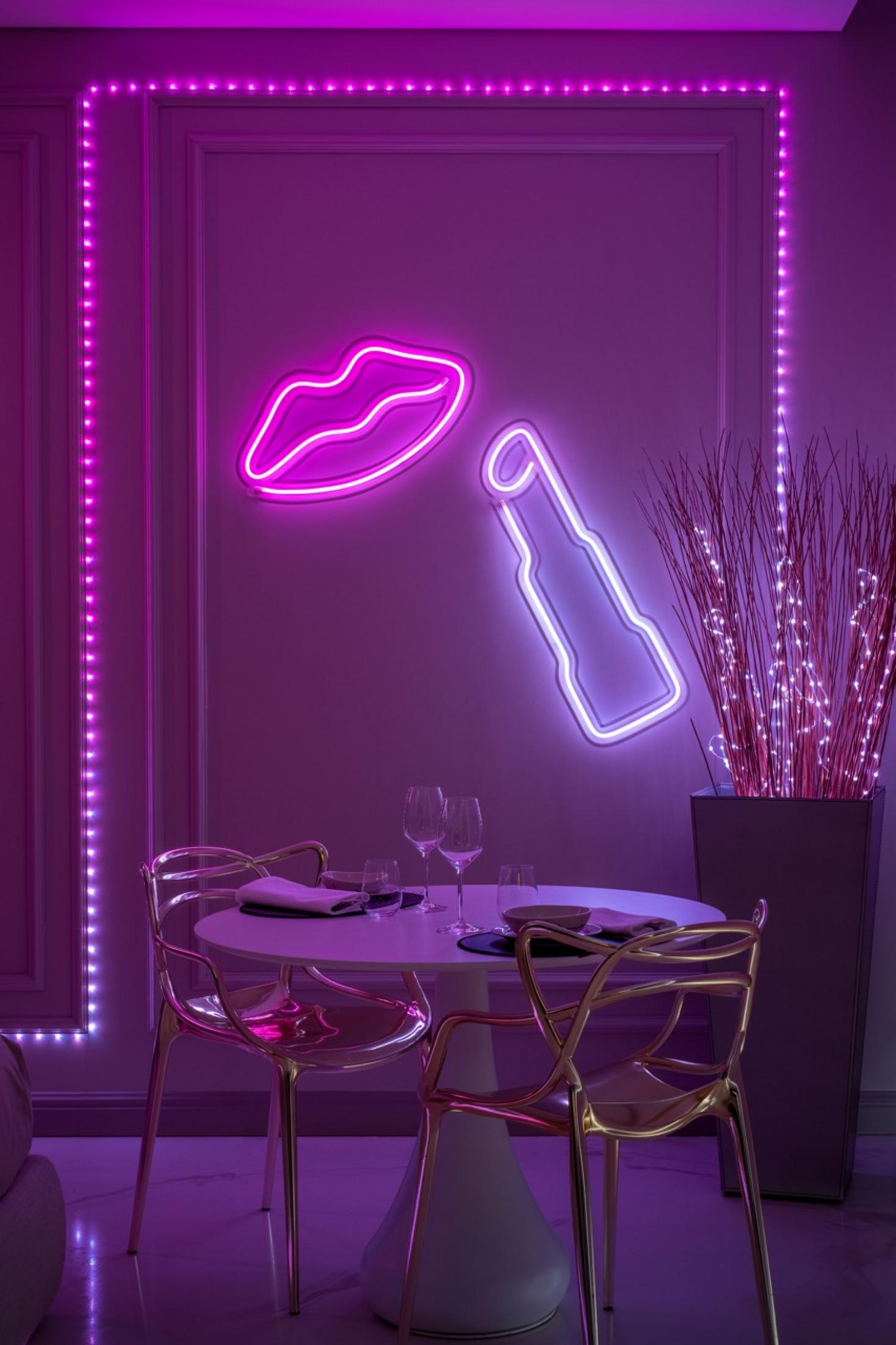Stół z krzesłami pod neonami w kształcie ust i szminki, oświetlony fioletowymi LED.