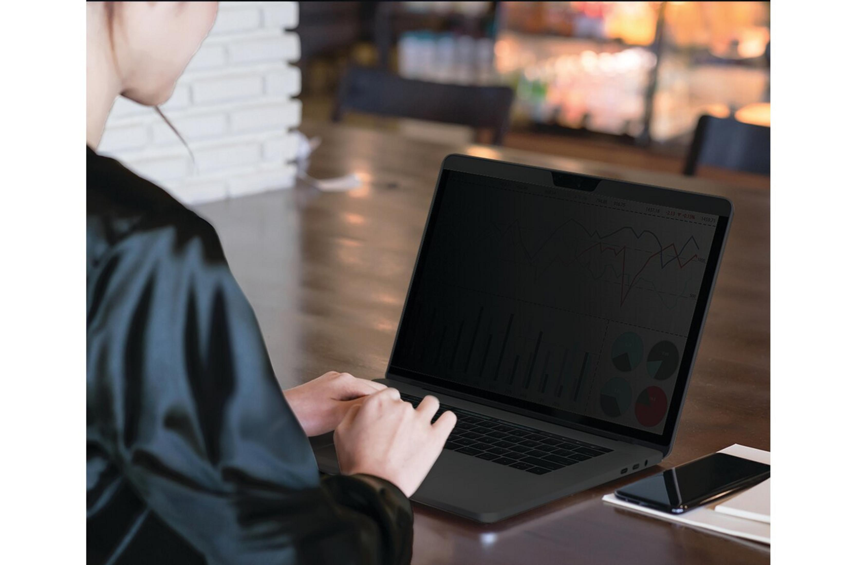 Eine Person in einem schwarzen Hemd tippt auf einem Laptop mit Finanzdiagrammen.