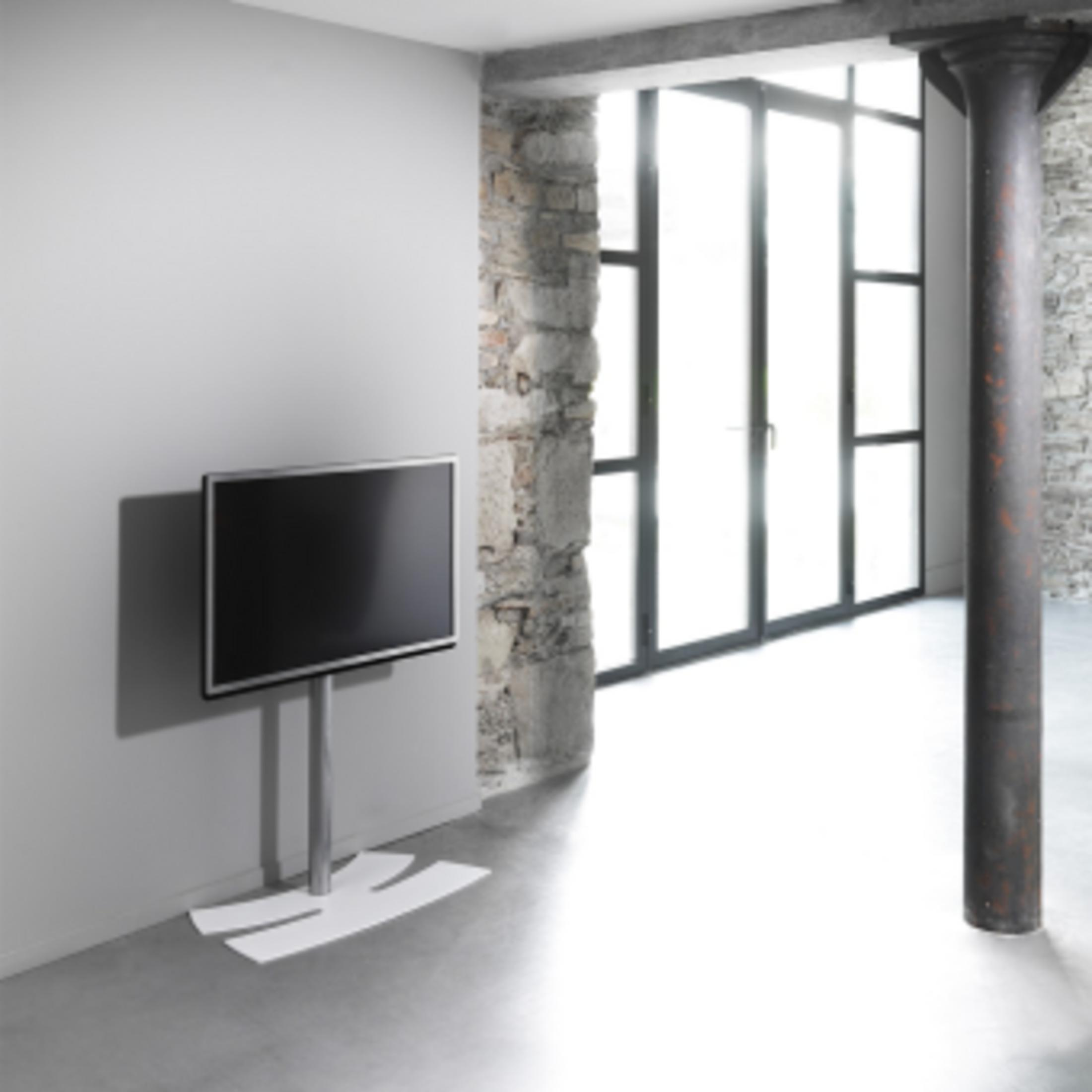 Una TV moderna su supporto davanti a una parete bianca. Grandi finestre sullo sfondo.