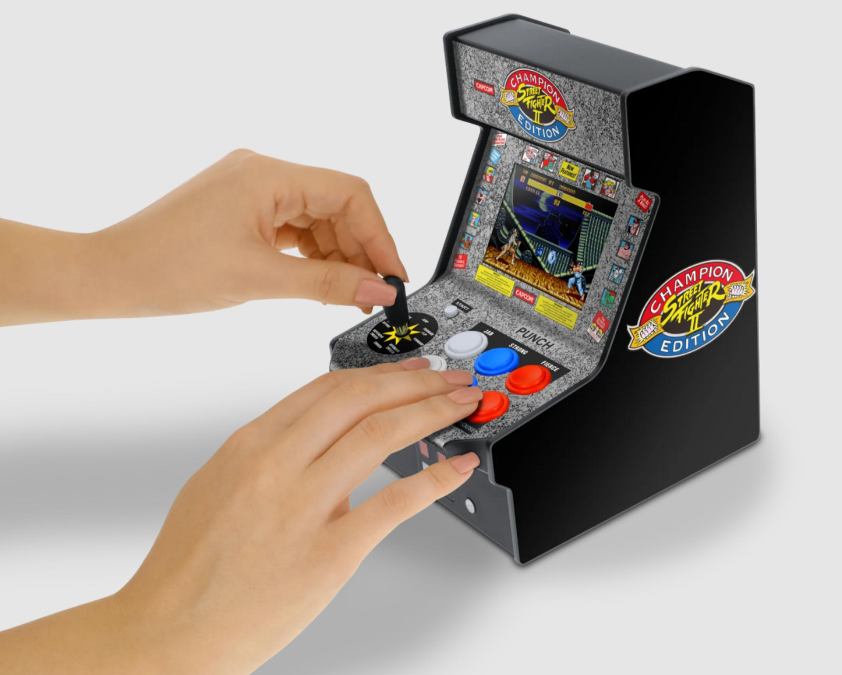 Una mano usa el joystick de una mini máquina arcade con gráficos de Street Fighter II.