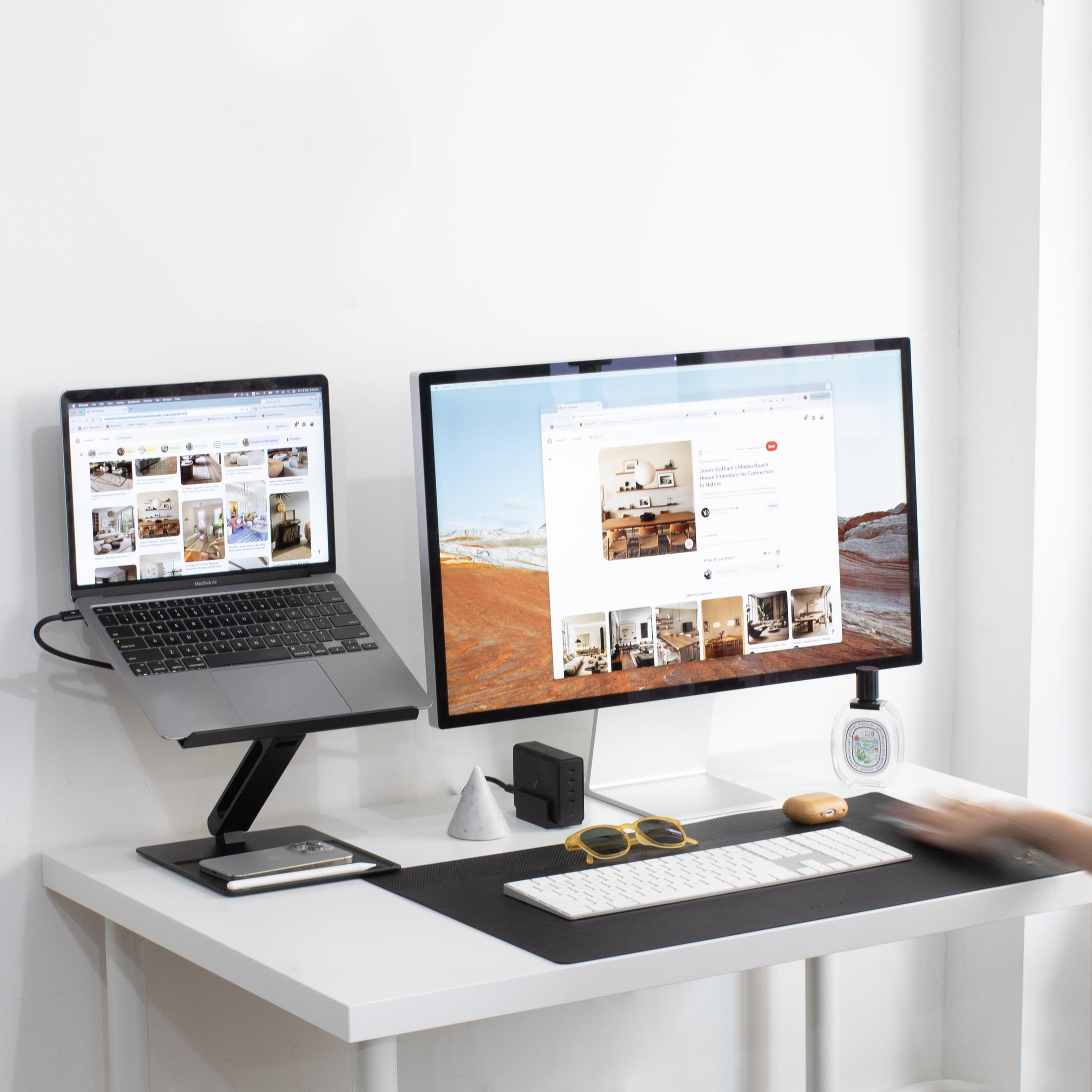 Una scrivania con laptop, monitor, tastiera e telefono. Decorazioni e una mano sono visibili.