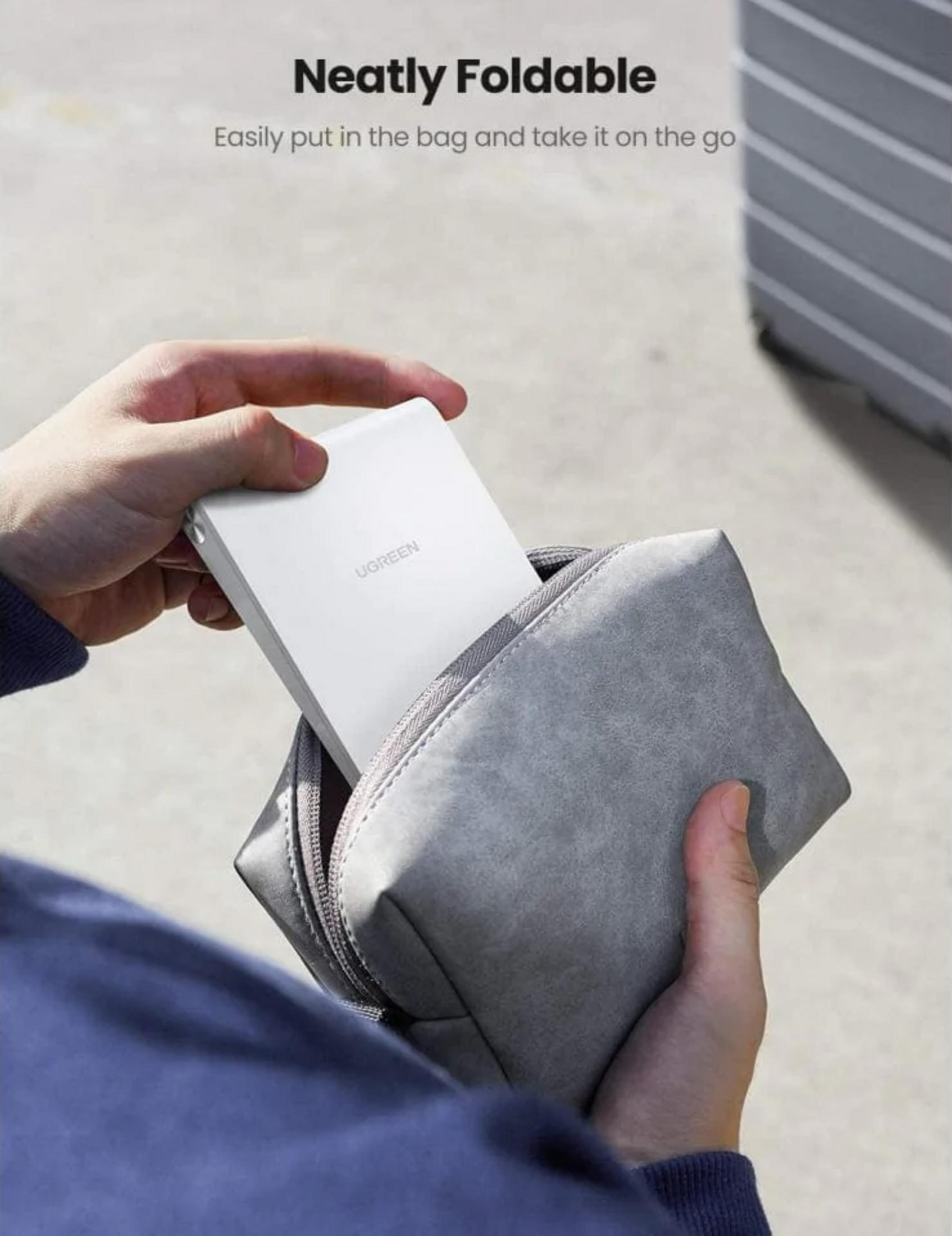 Eine Hand legt ein weißes UGREEN-Gerät in eine graue Tasche.
