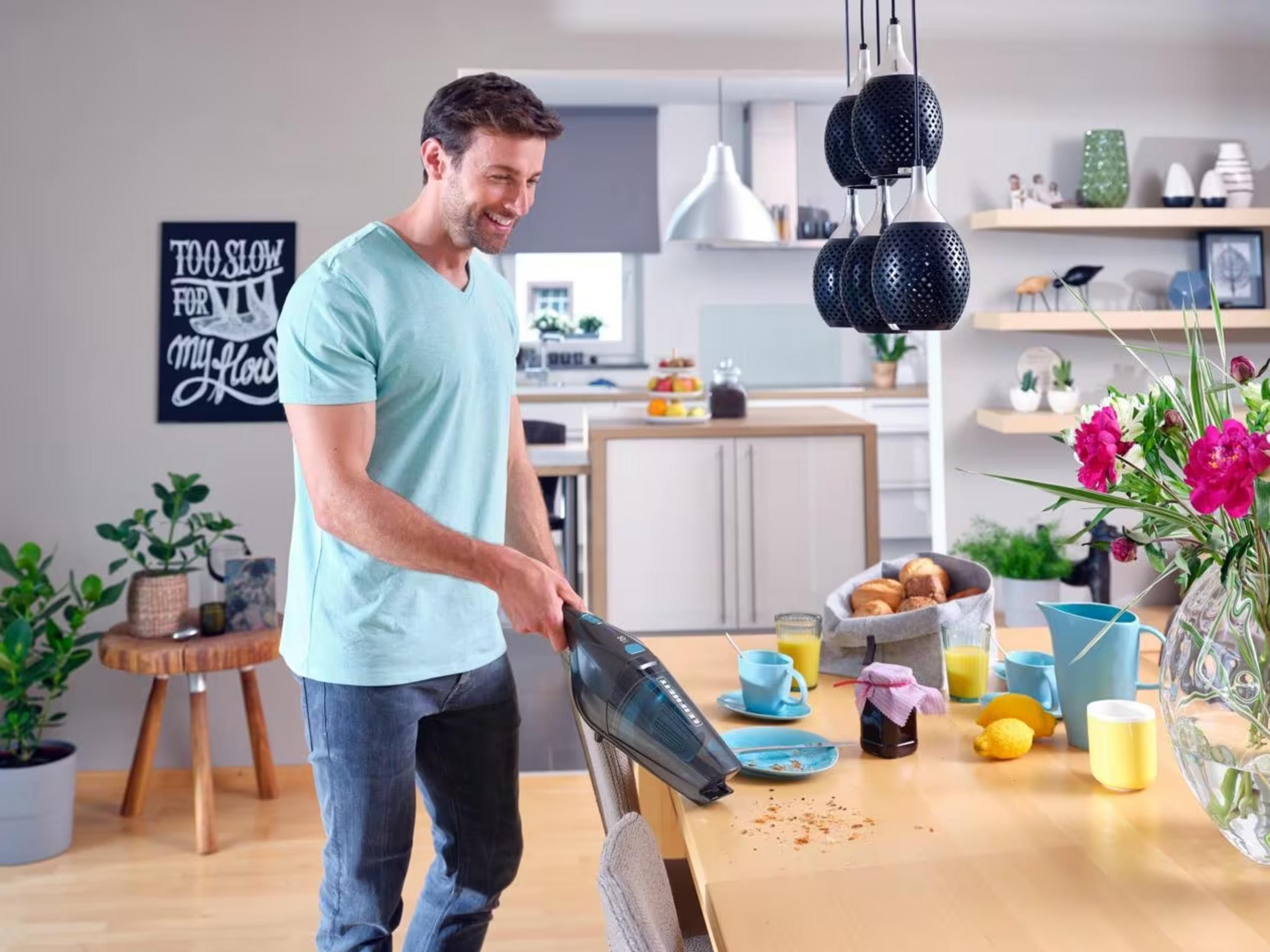 Mężczyzna odkurza okruchy ze stołu odkurzaczem ręcznym. Artykuły śniadaniowe na stole.