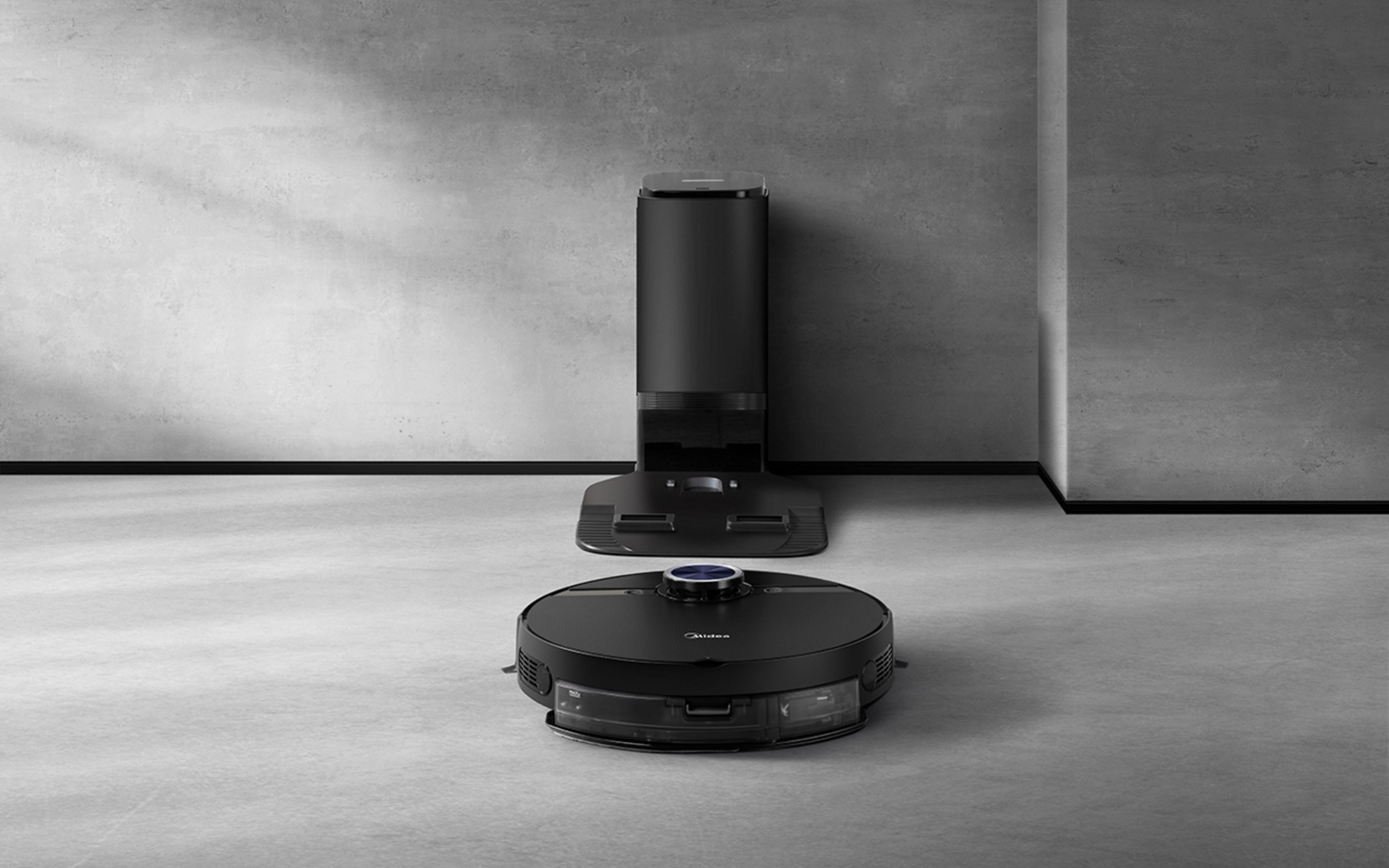 Un robot aspirador negro está frente a una estación de carga negra contra una pared de hormigón.
