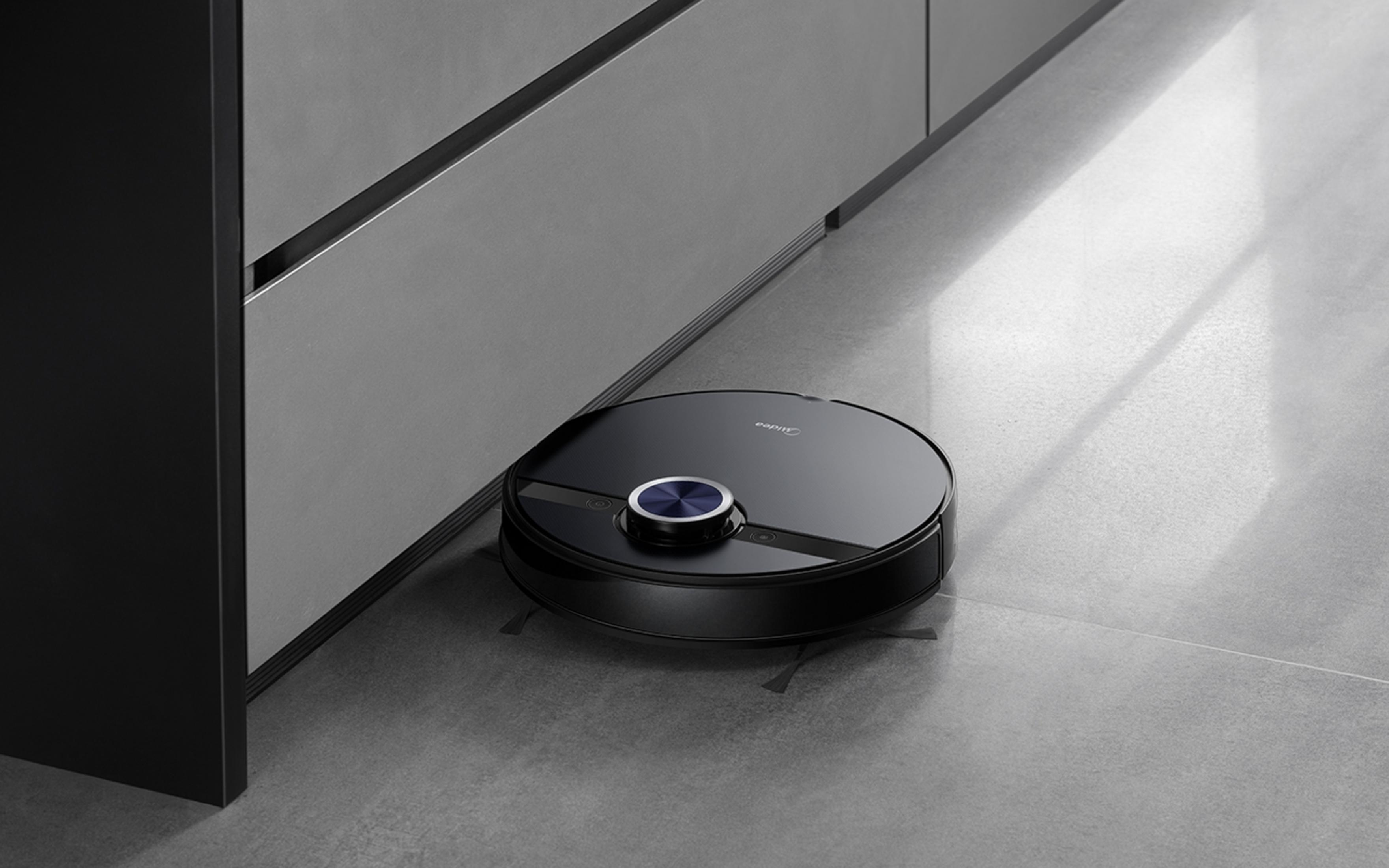 Un robot aspirador redondo negro con centro azul está en un suelo gris.