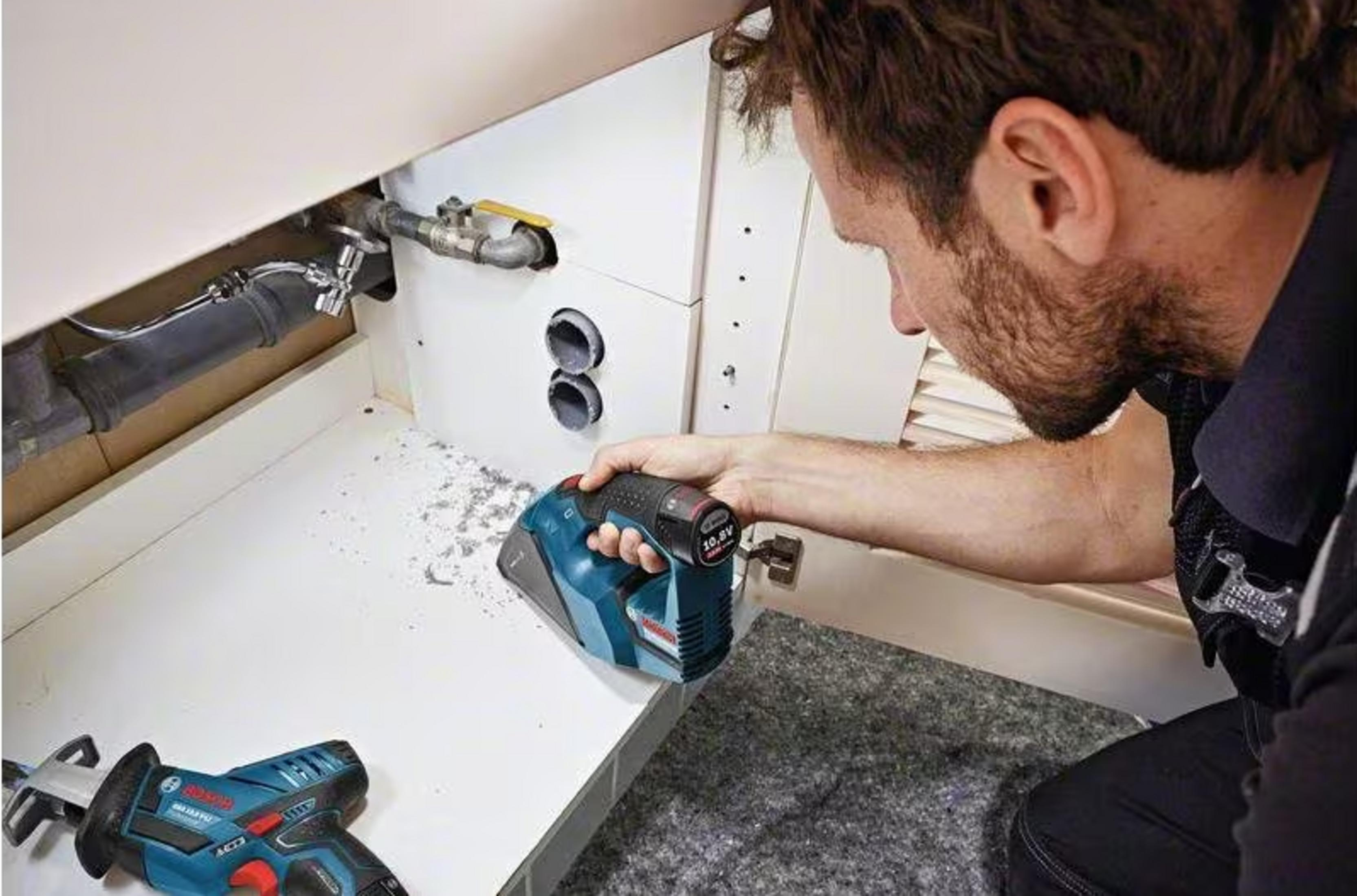 Hombre trabaja en tuberías bajo el lavabo con herramientas. Herramientas y escombros esparcidos.